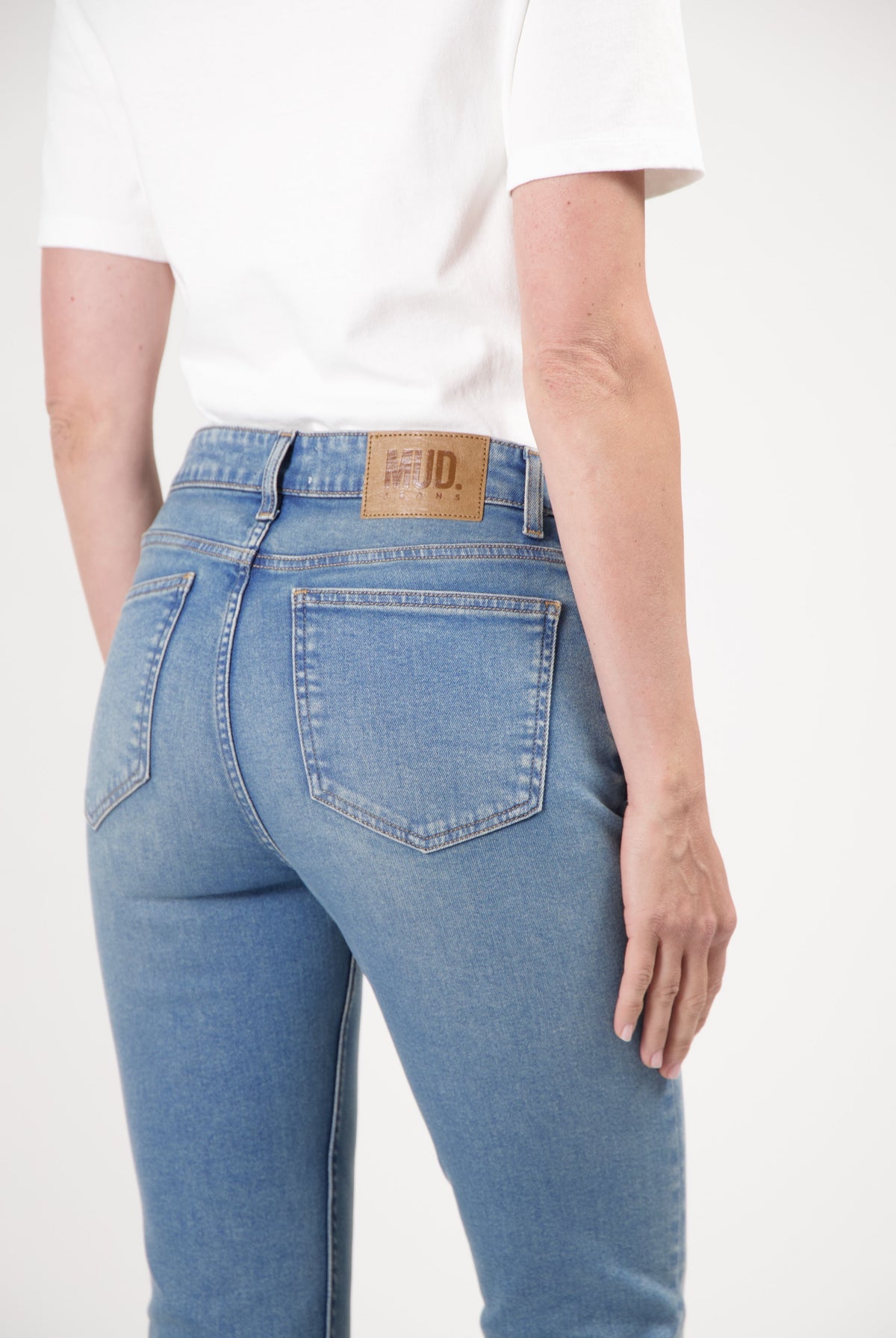 Person wearing sustainable MUD Jeans in a light blue wash, showcasing a back view with a white short-sleeve top.