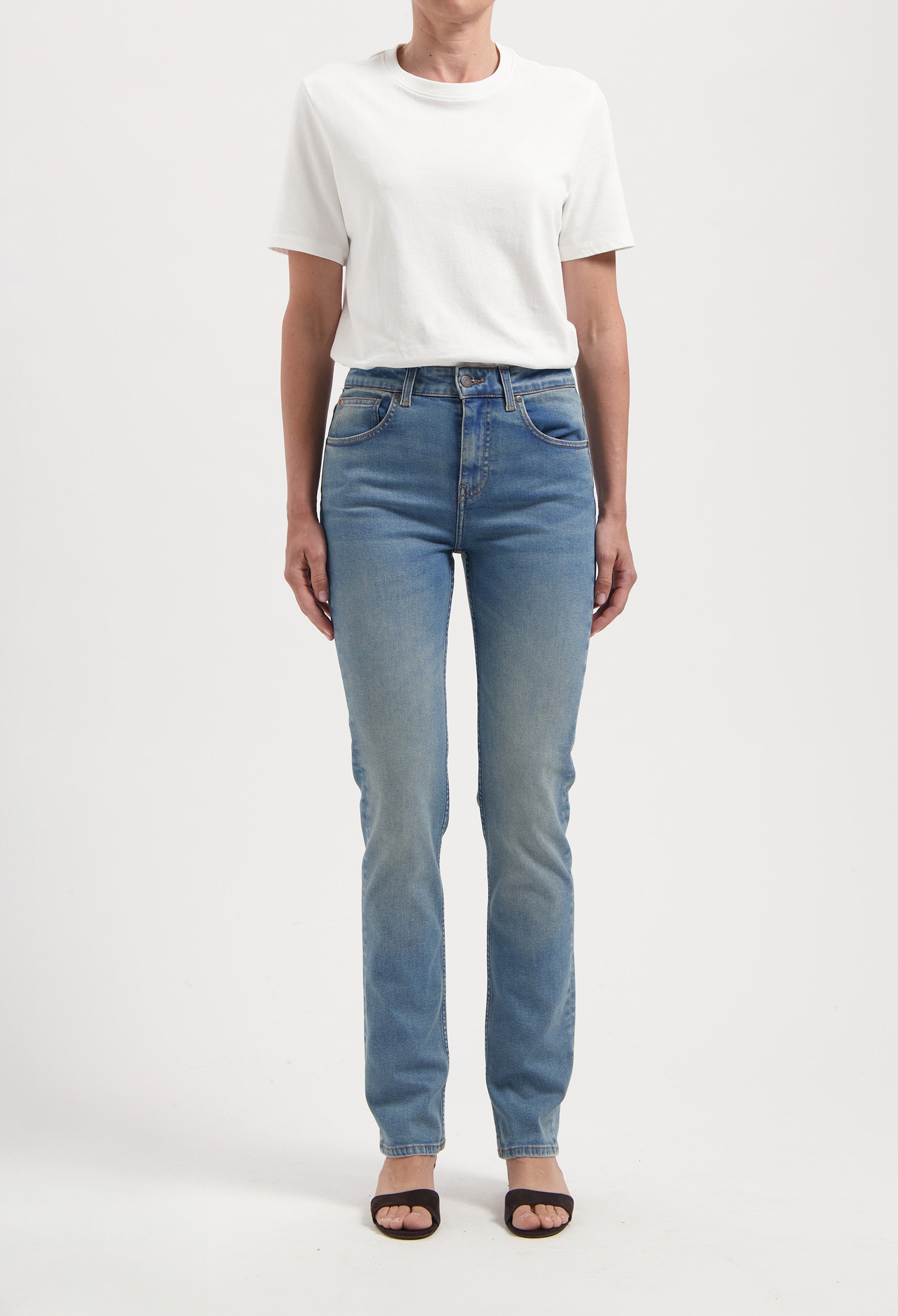 Casual outfit featuring a plain white short-sleeve top and high-waisted light blue jeans with front pockets, styled with black sandals.
