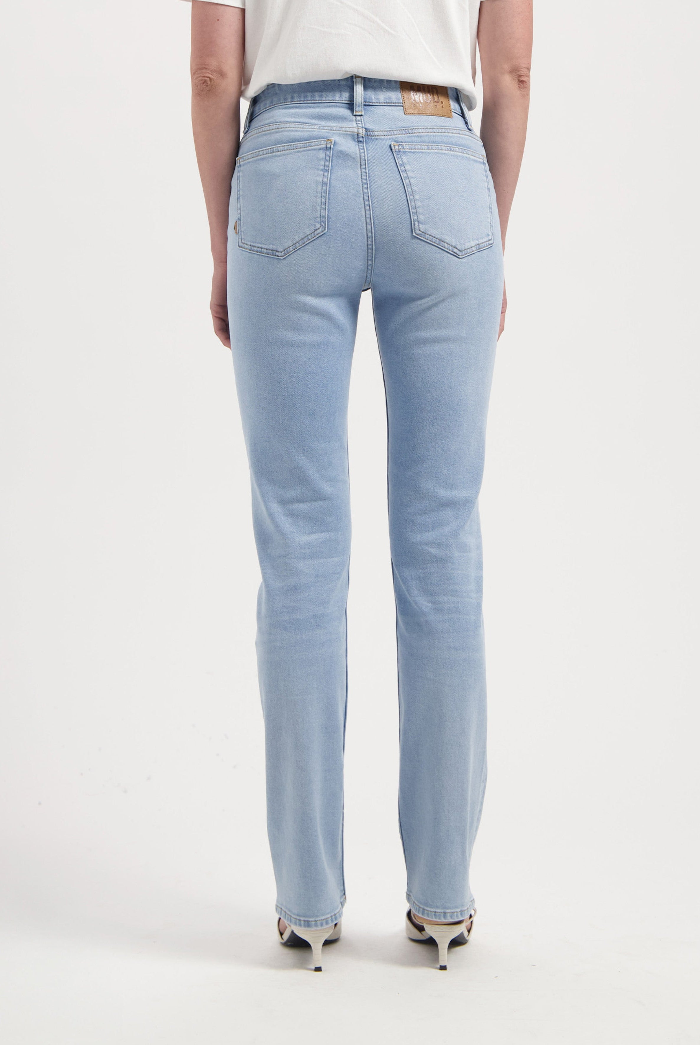 Light blue, straight-leg denim jeans made from organic cotton, shown from the back, paired with white heels and a T-shirt.