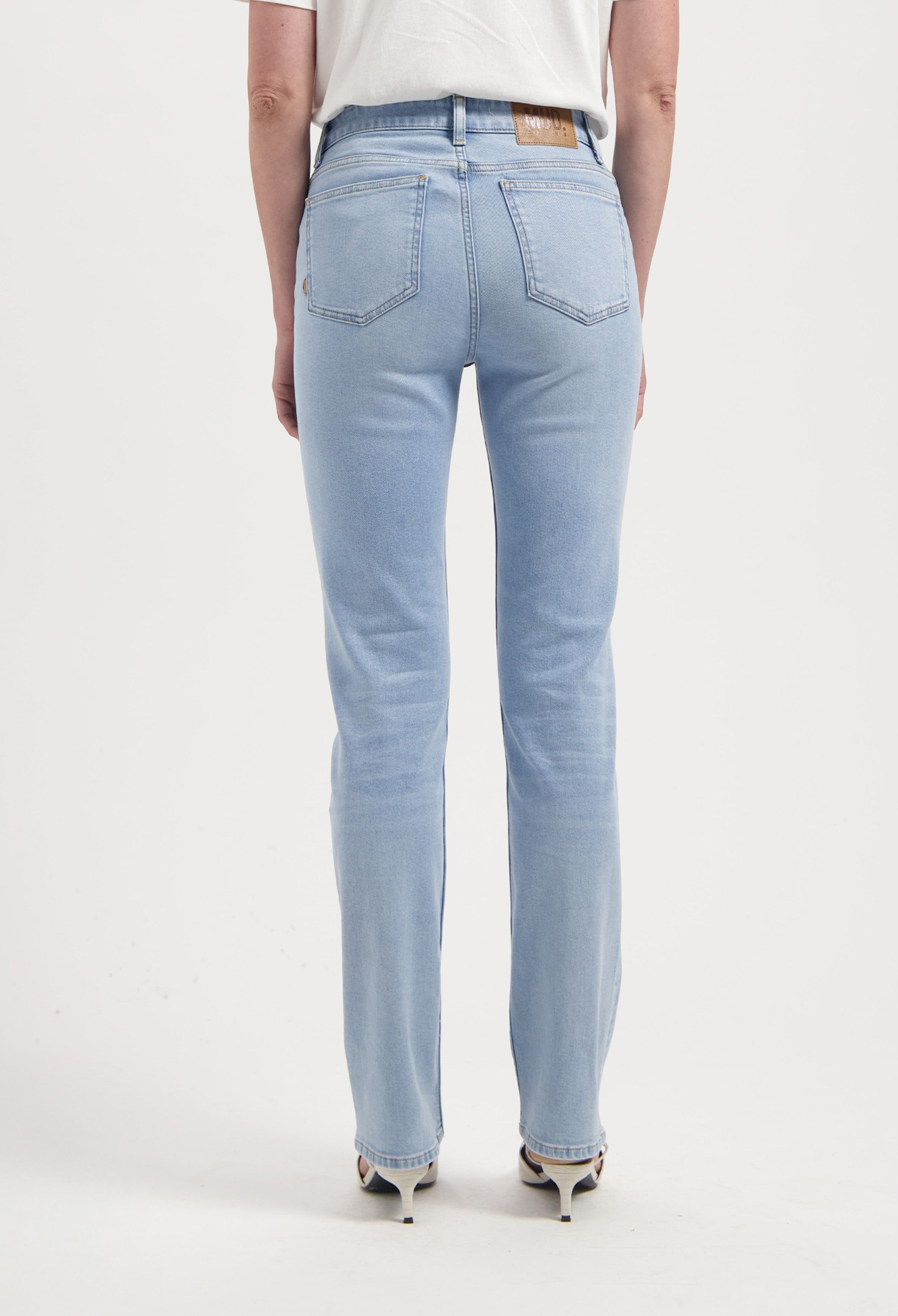 Light blue, straight-leg denim jeans made from organic cotton, shown from the back, paired with white heels and a T-shirt.