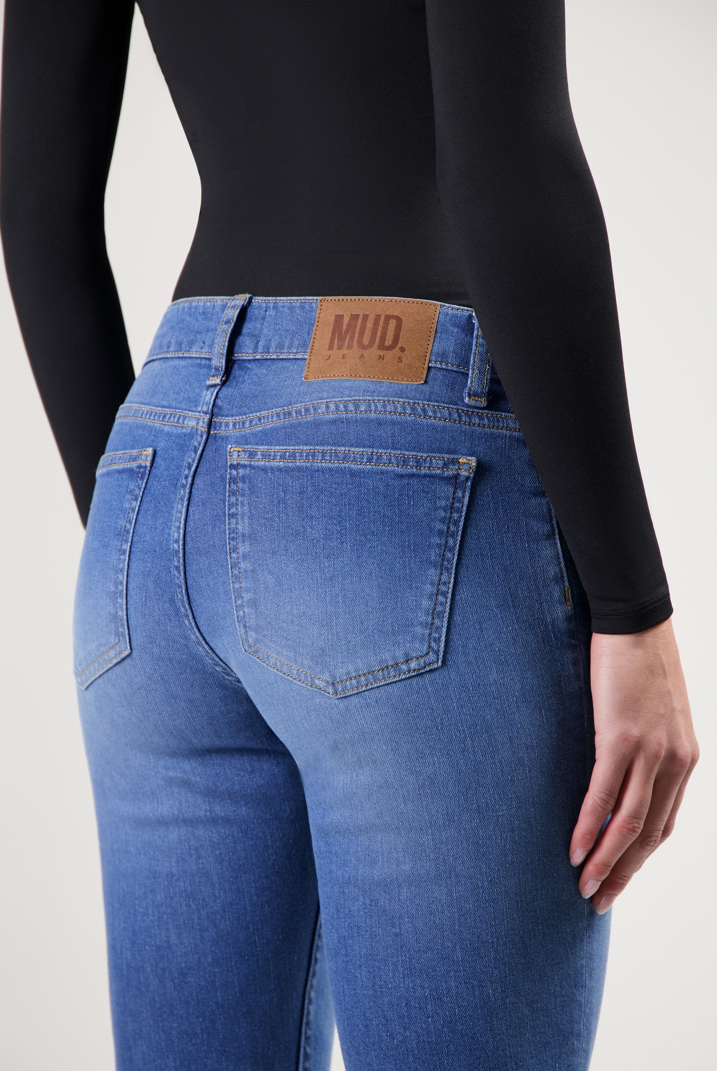 Dark blue MUD Jeans made from organic cotton, showing close-up of back pocket with tan leather patch, worn with a black top.