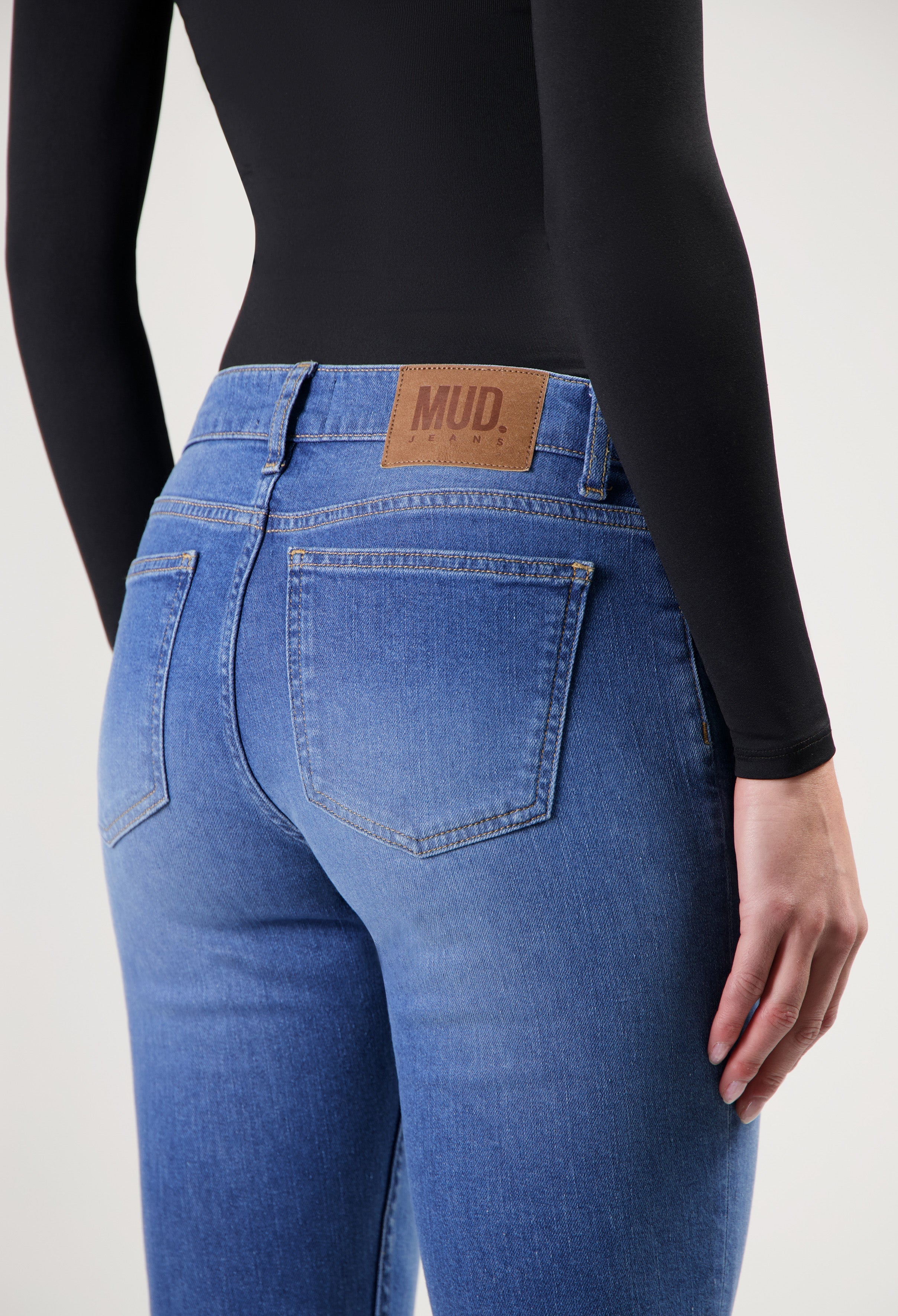 Dark blue MUD Jeans made from organic cotton, showing close-up of back pocket with tan leather patch, worn with a black top.