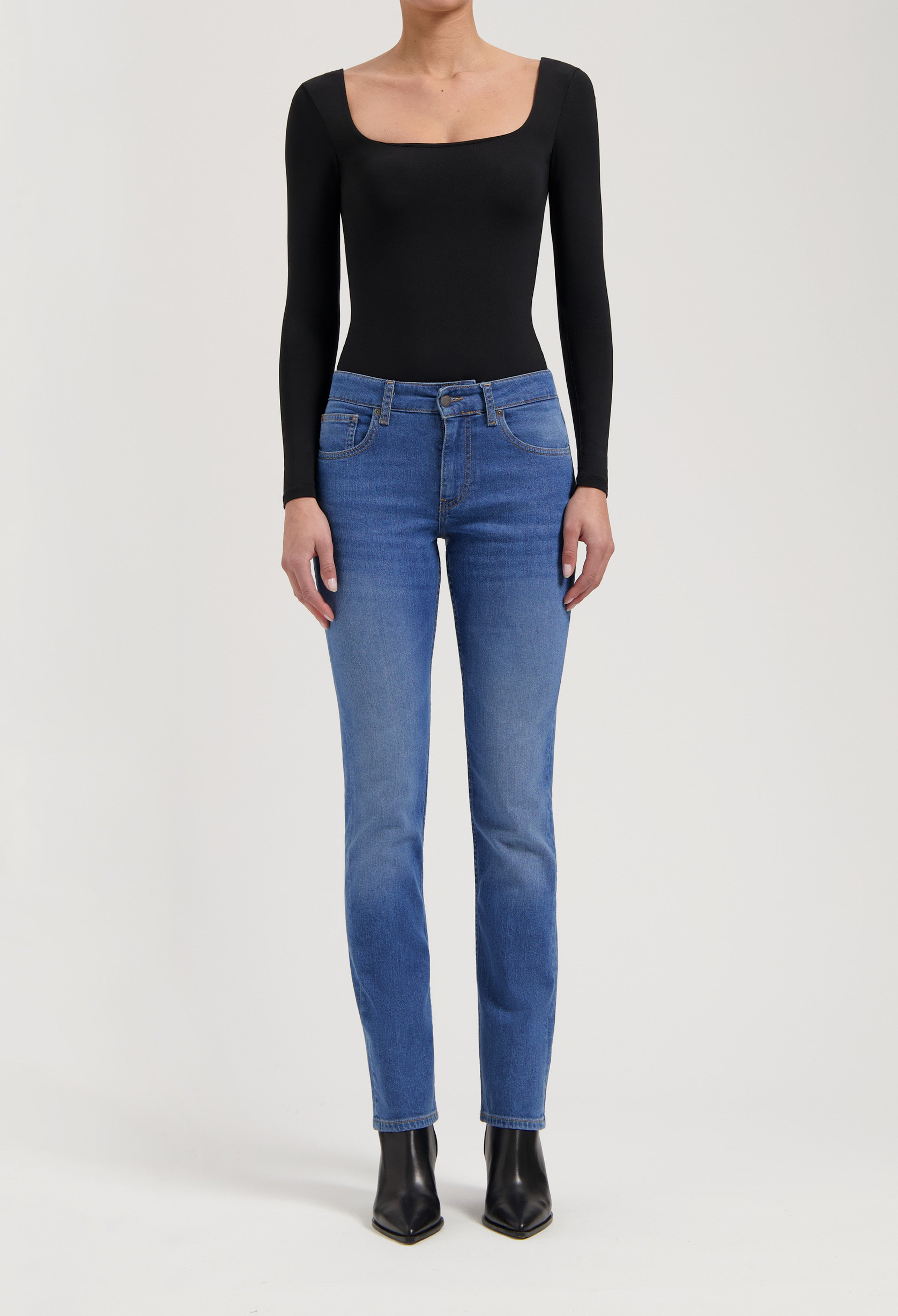 Woman in blue straight-leg jeans and a fitted black scoop-neck top with long sleeves, paired with black ankle boots.
