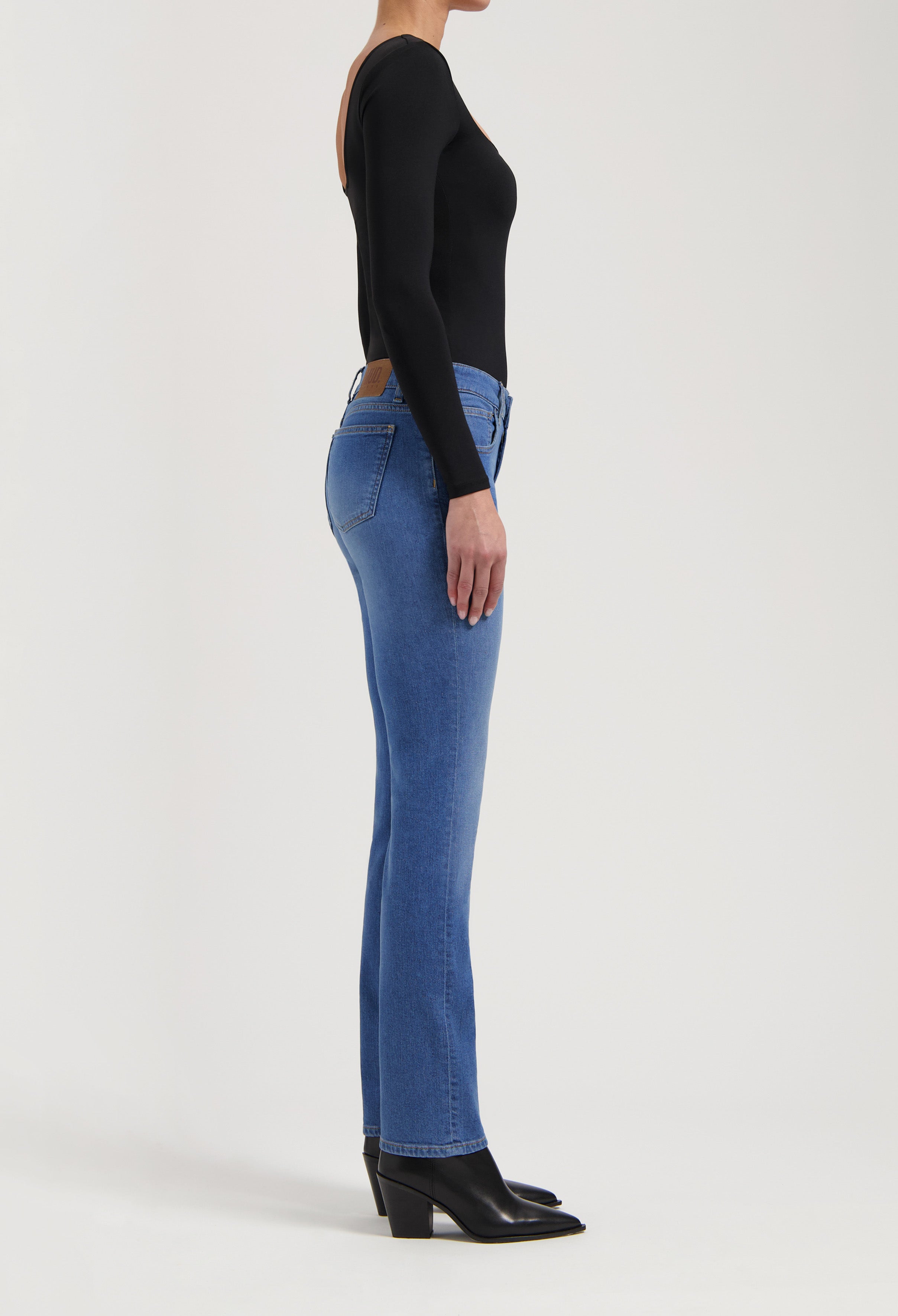 Side view of woman in fitted blue MUD jeans paired with black long-sleeve top and heeled boots, highlighting sleek silhouette.