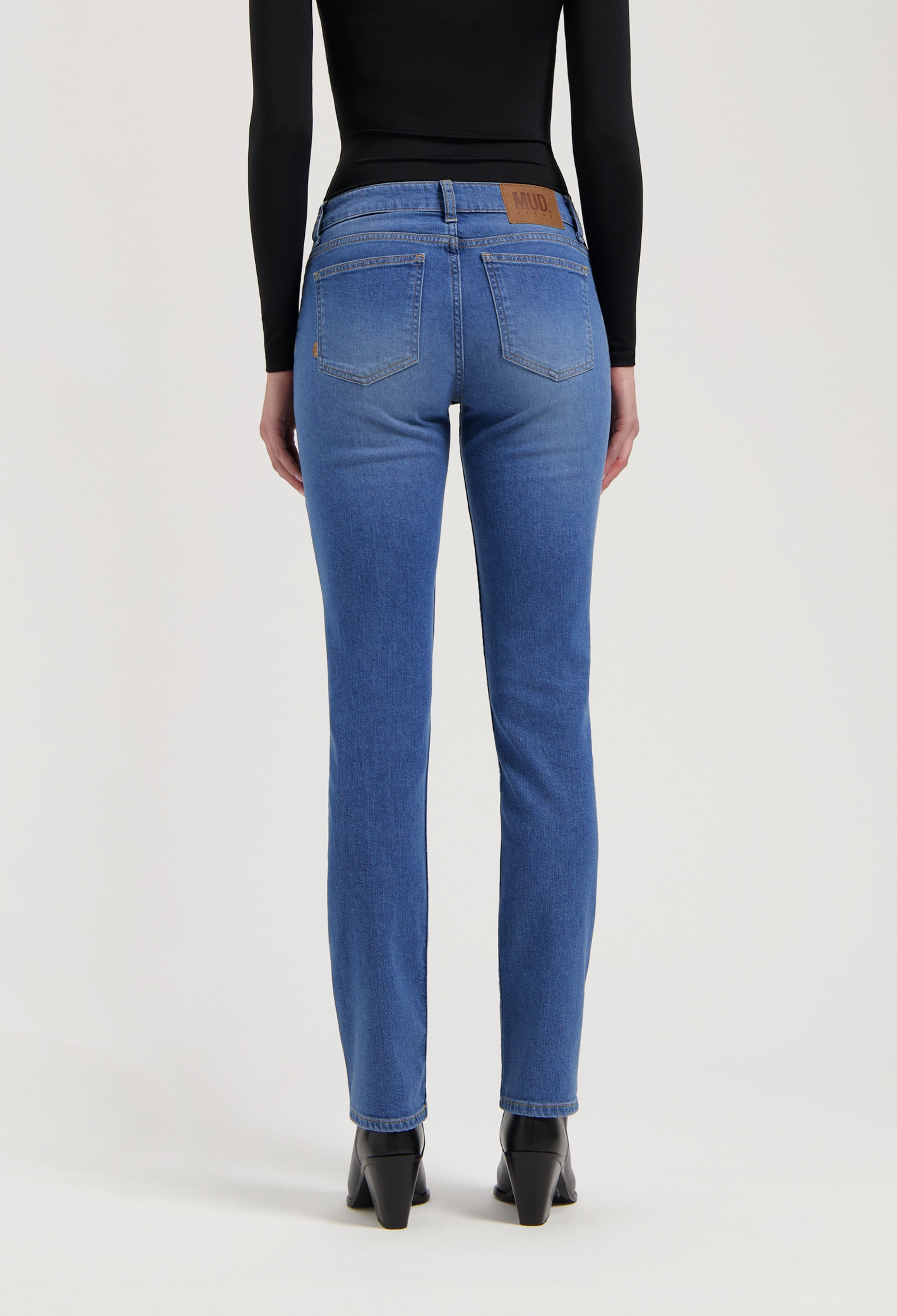 Rear view of sustainable MUD Jeans, blue straight-fit denim, worn with a long-sleeve black top and black boots.