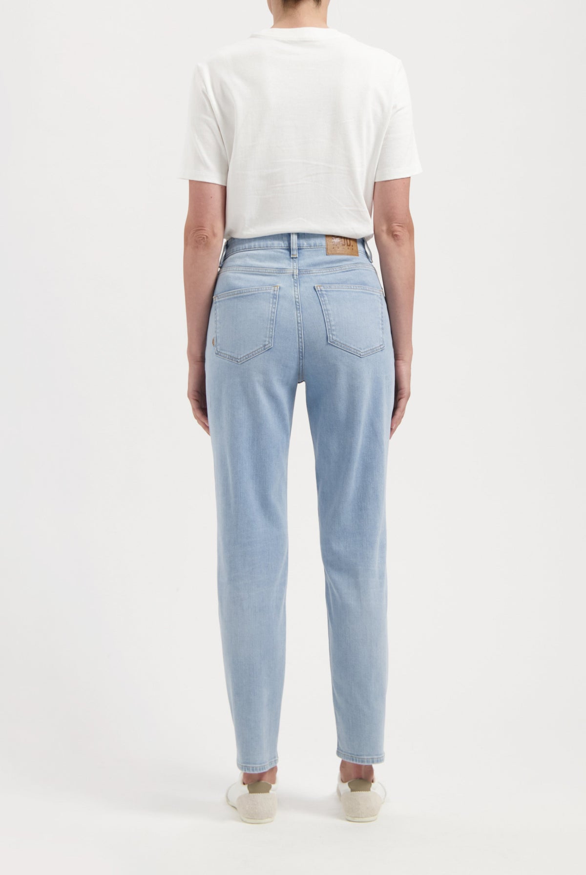 Back view of a person wearing light blue, straight-leg jeans paired with a white short-sleeve top, showcasing casual style.