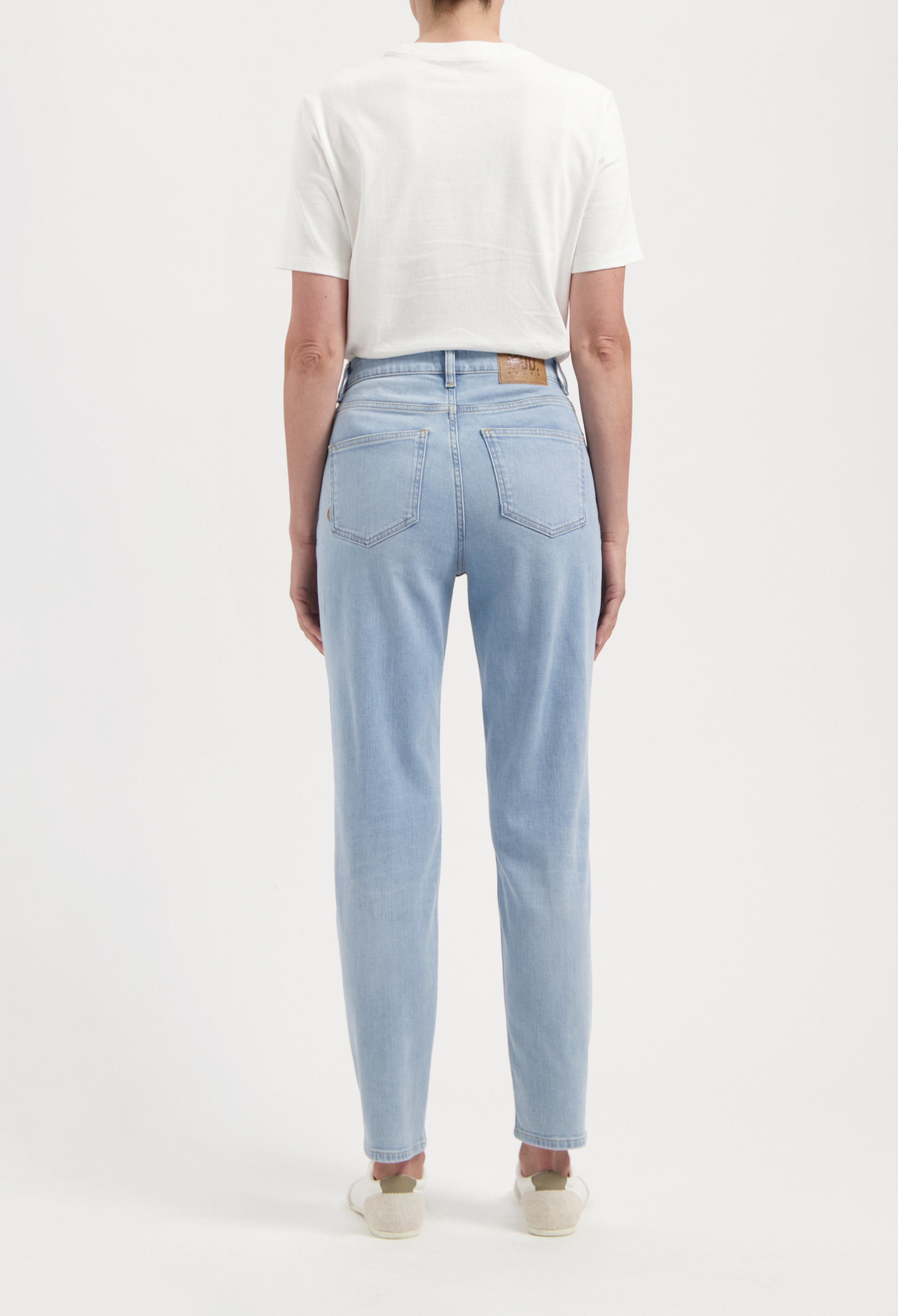 Back view of a person wearing light blue, straight-leg jeans paired with a white short-sleeve top, showcasing casual style.