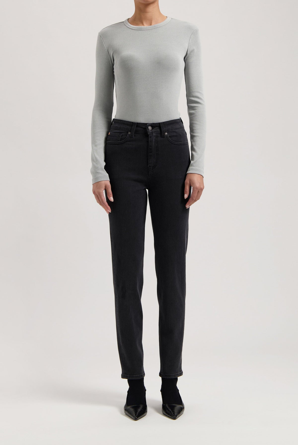 Gray long-sleeve top paired with high-waisted black jeans and pointed black shoes, showcasing a modern minimalist outfit.