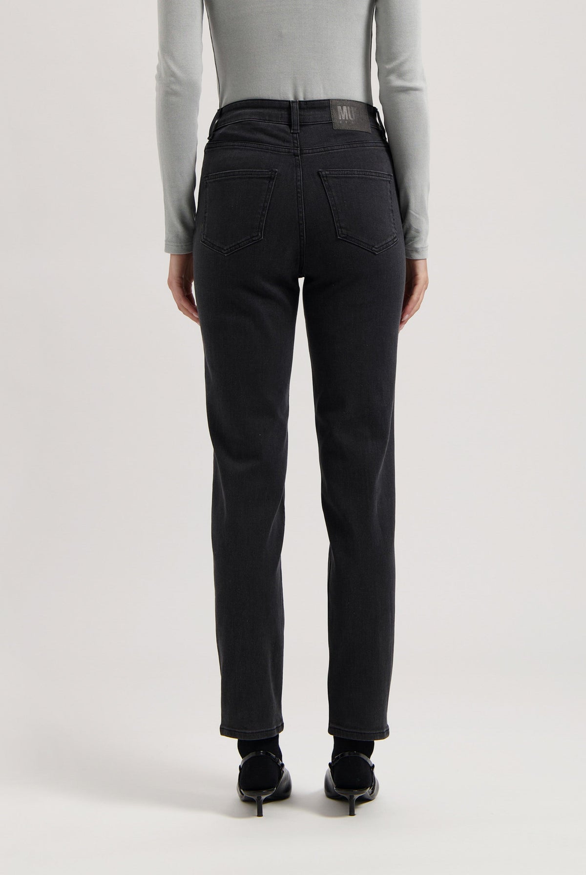 Back view of black, high-waisted denim jeans worn with a fitted gray long-sleeve top, showcasing modern casual fashion.