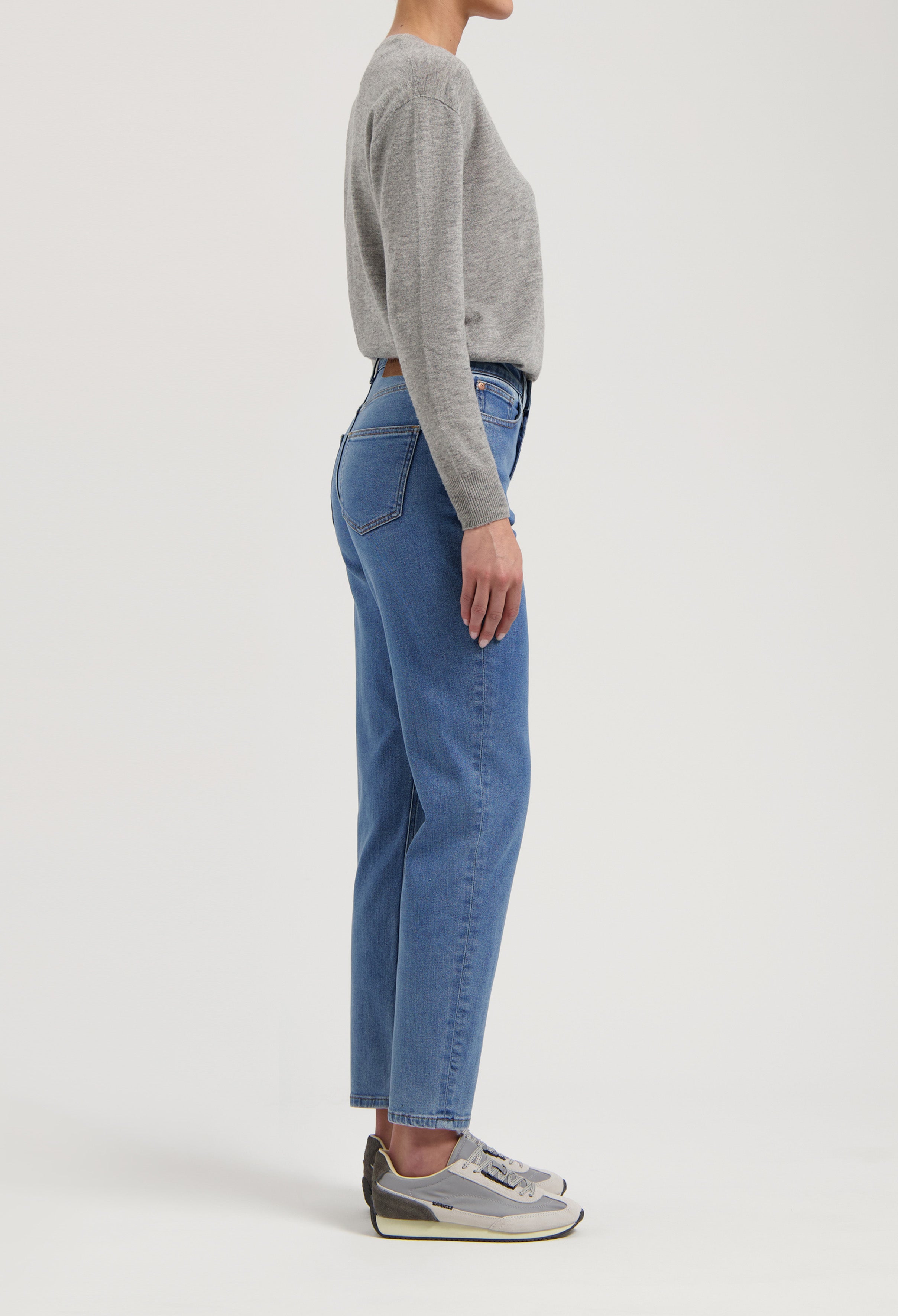 Gray knit sweater paired with blue high-waisted denim jeans and gray sneakers in a side profile view.