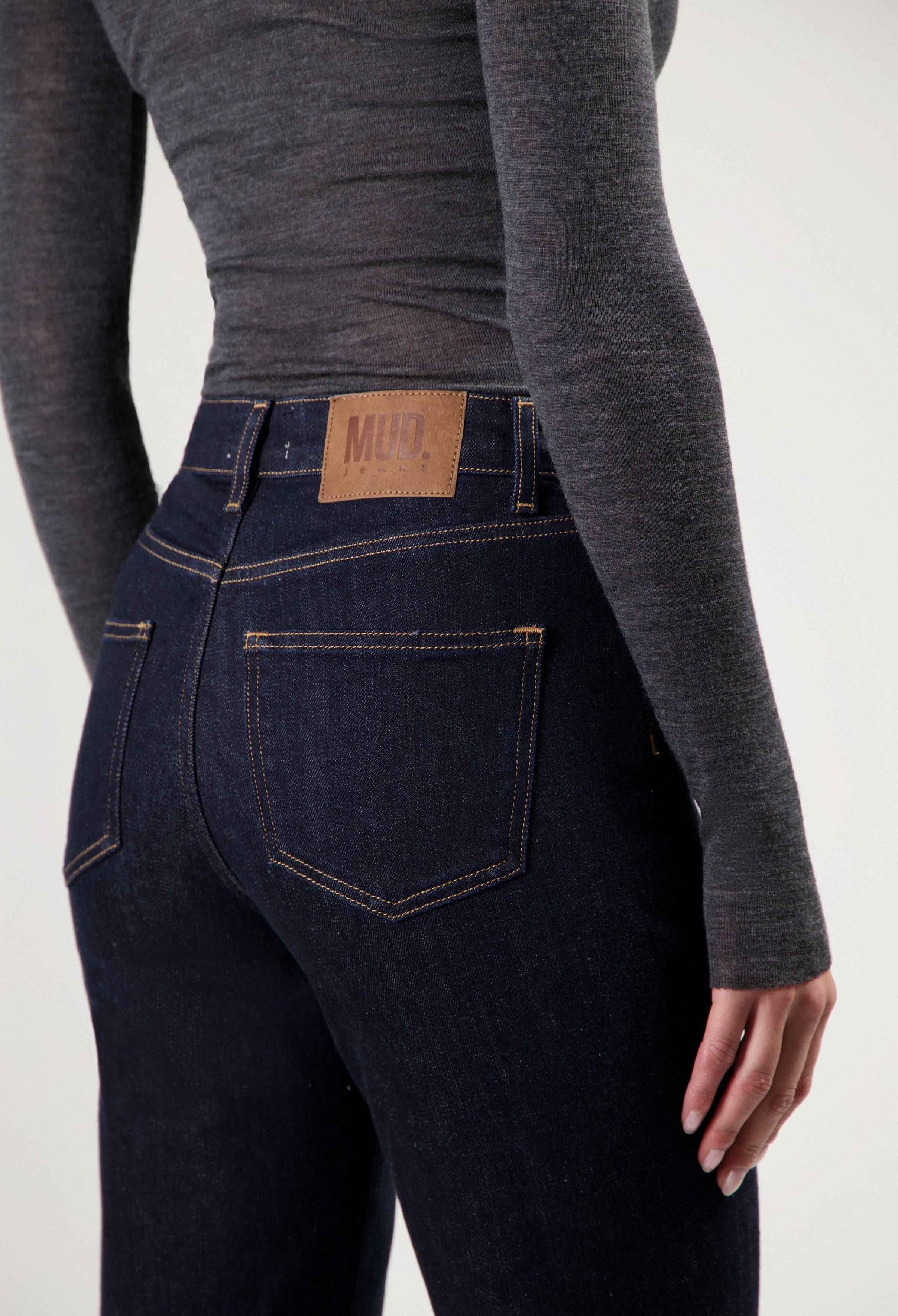 Dark blue sustainable denim jeans in a slim-fit style with contrasting stitching, paired with a sleek gray long-sleeve top.