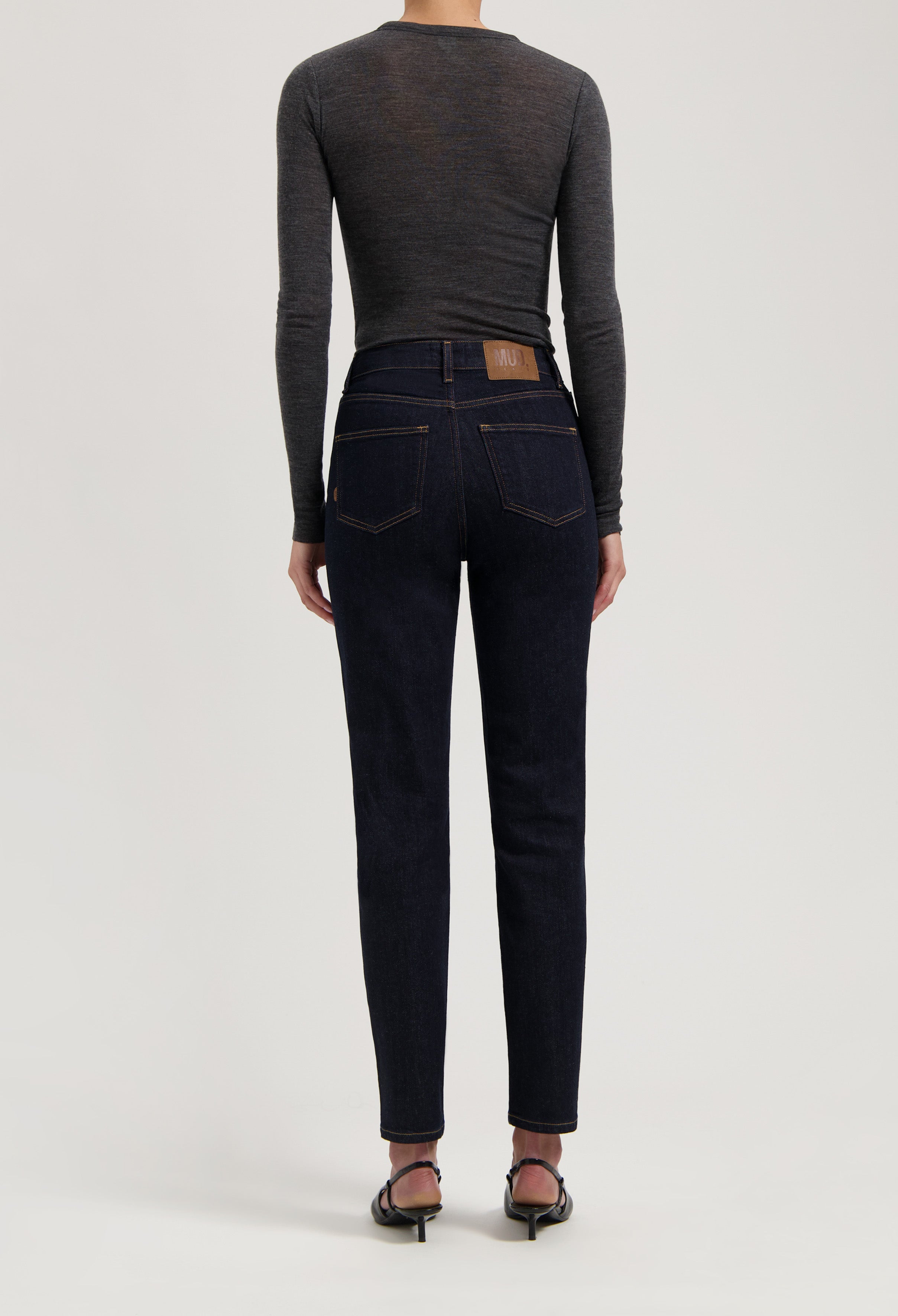 Dark blue MUD Jeans made from organic cotton, featuring a high-waisted, straight fit, worn with a long-sleeve gray shirt.