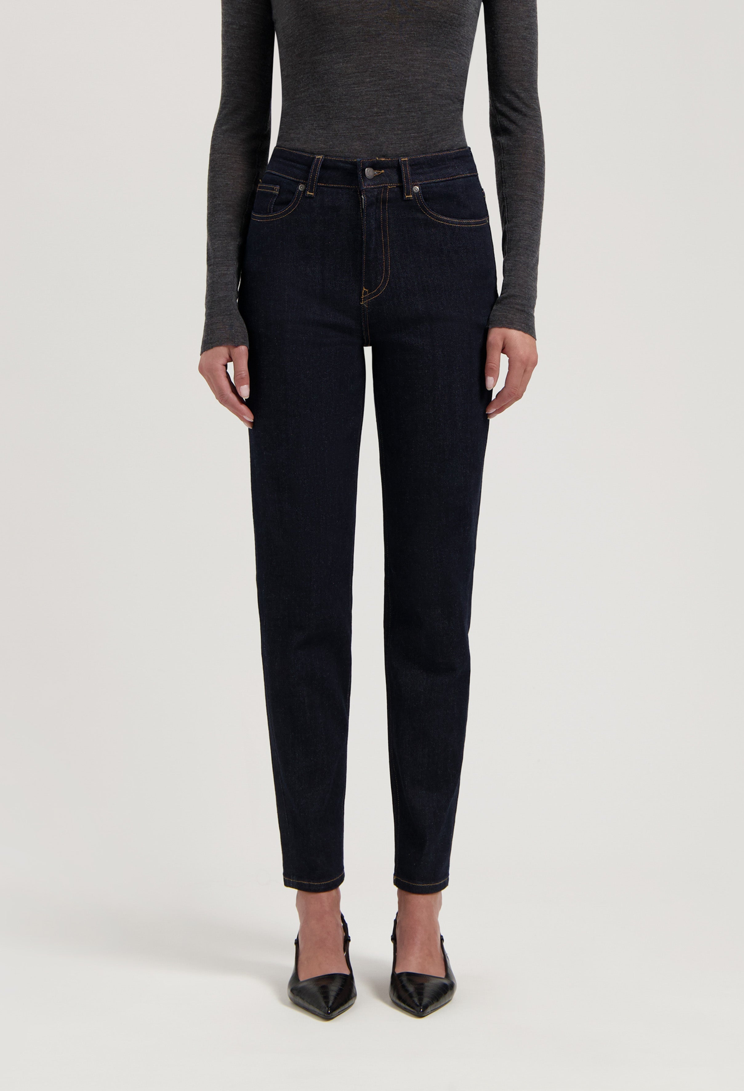 Dark blue, slim-fit jeans made from organic cotton, paired with a form-fitting long-sleeve gray top and black heels.