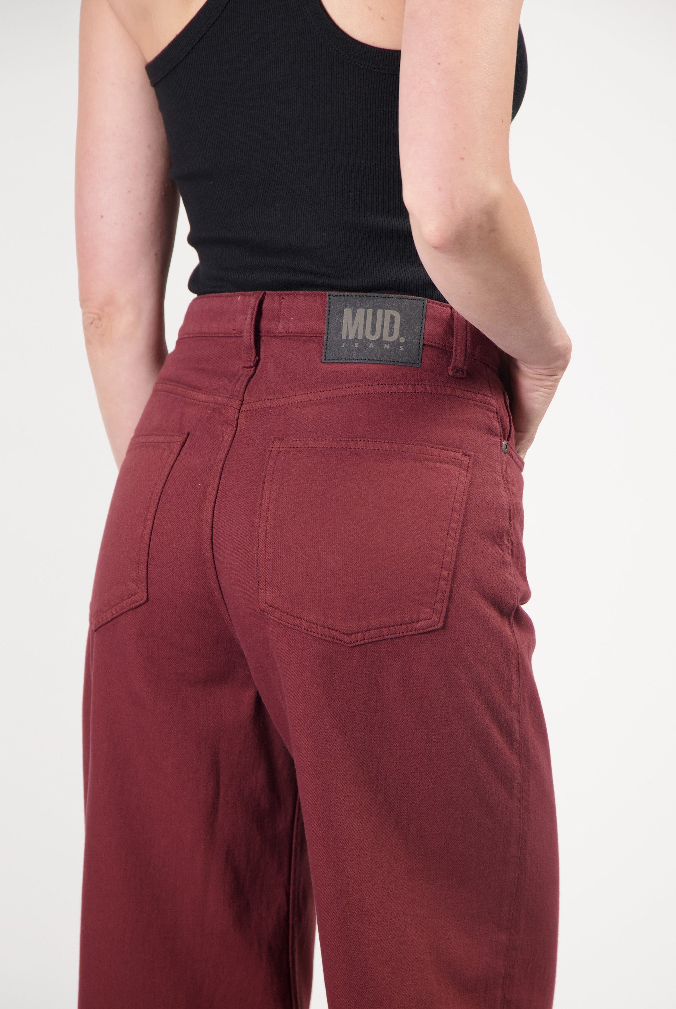 Organic cotton MUD Jeans in deep red, showcasing high-waisted fit with back pockets, paired with a black tank top.