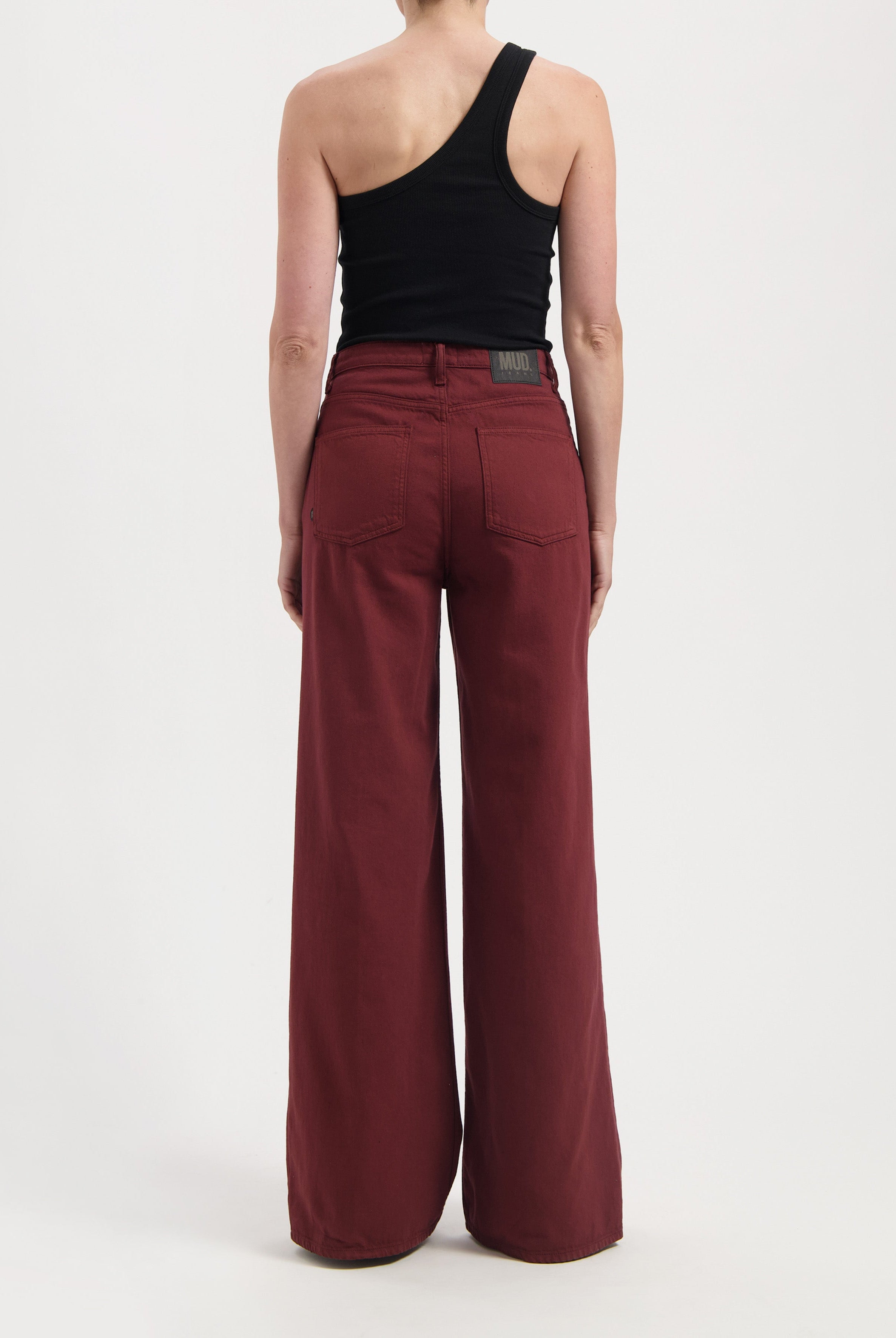 Wide-leg burgundy jeans made from sustainable organic cotton, paired with a modern black one-shoulder tank top.