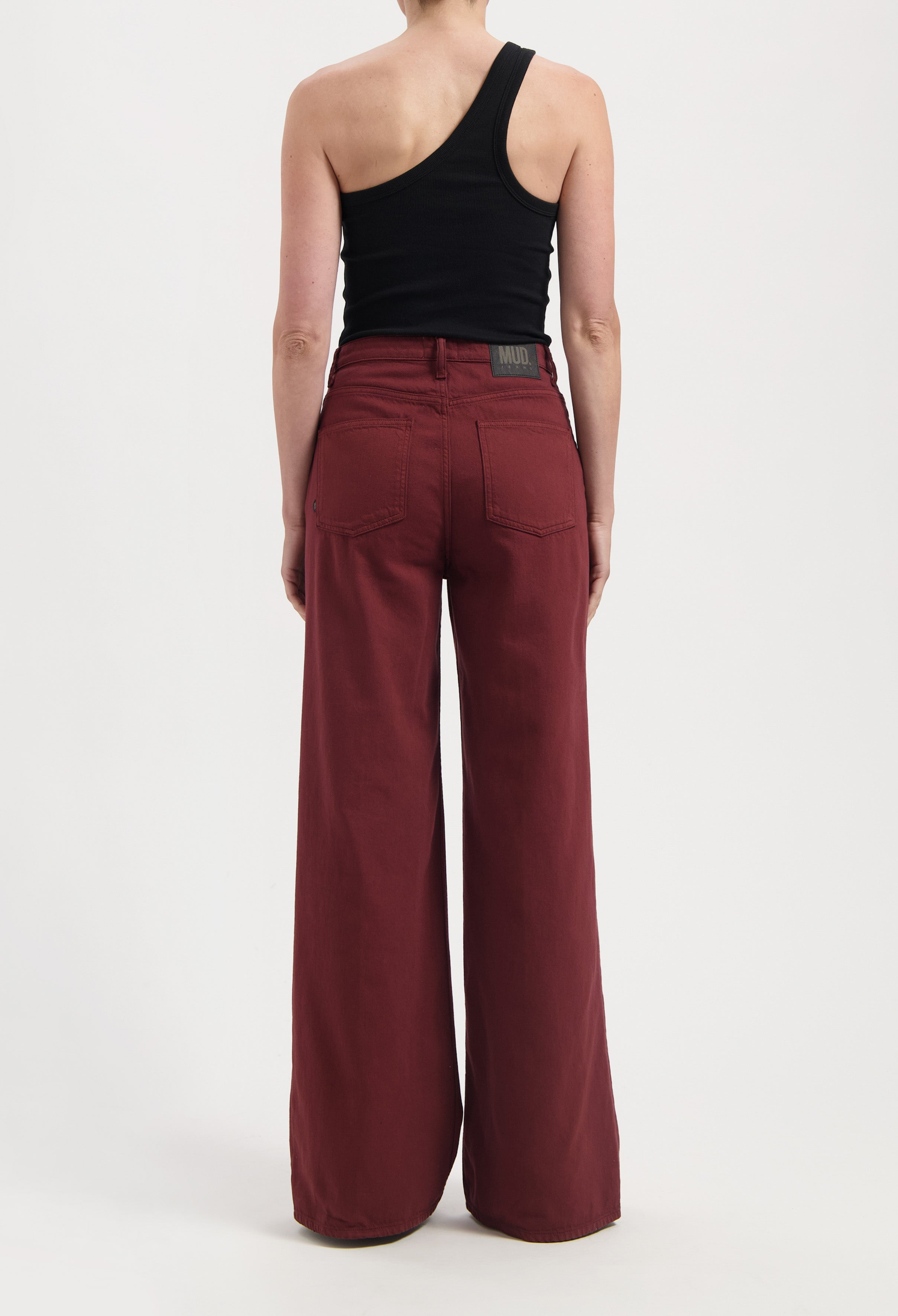 Wide-leg burgundy jeans made from sustainable organic cotton, paired with a modern black one-shoulder tank top.