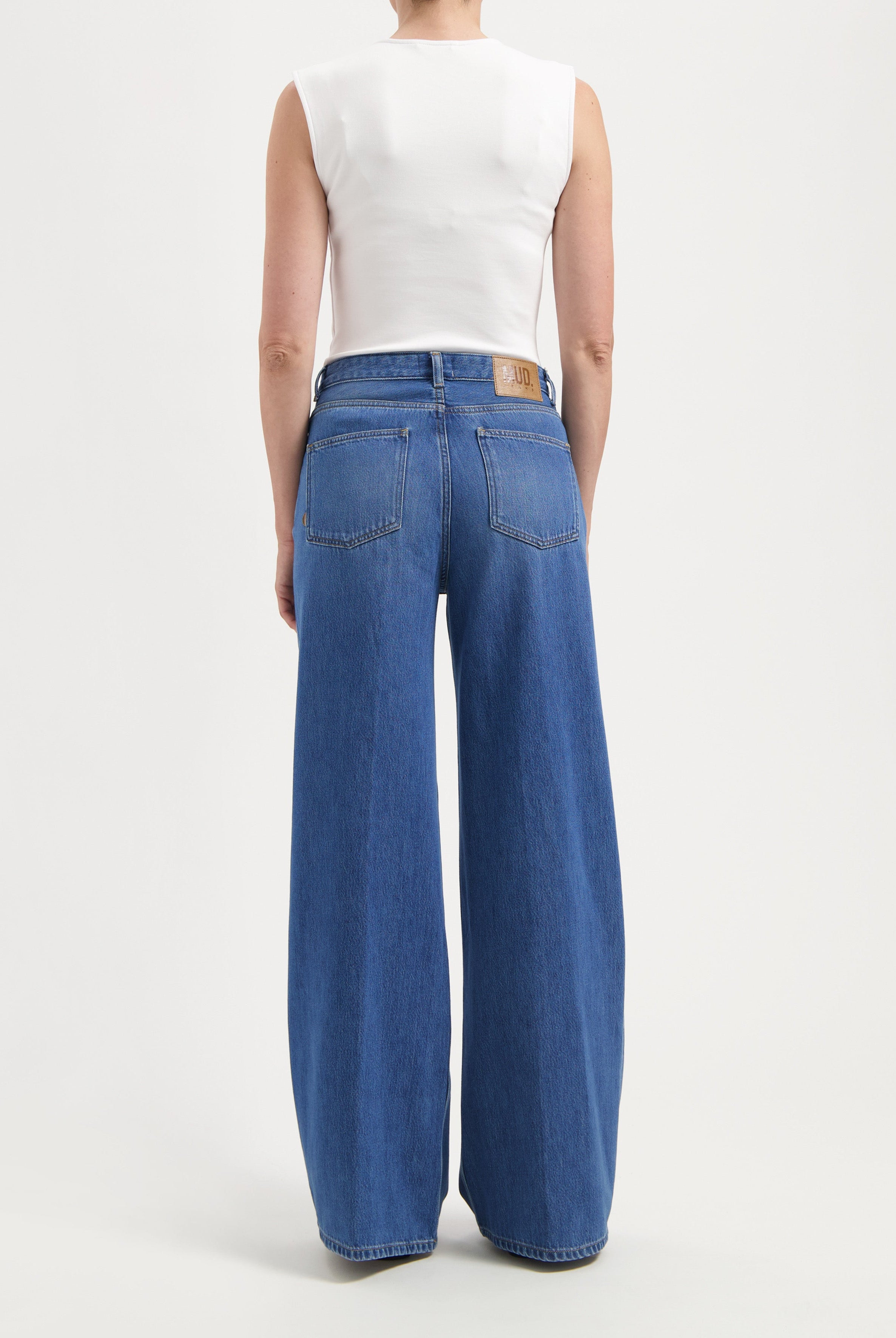 High-waisted wide-leg jeans in classic blue denim, worn with a sleeveless white top, showcasing casual style.