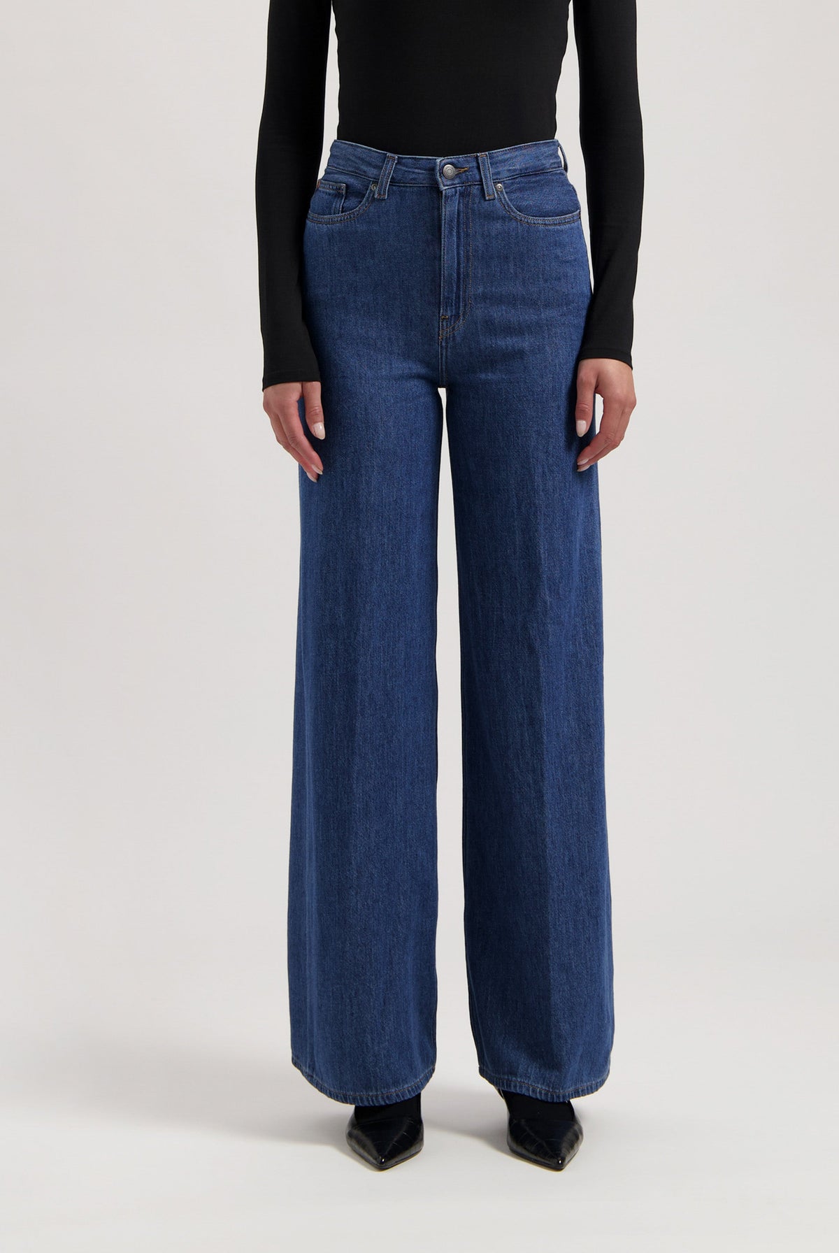 Wide-leg blue jeans in soft denim, paired with a black long-sleeve top; high-waisted with front button closure.