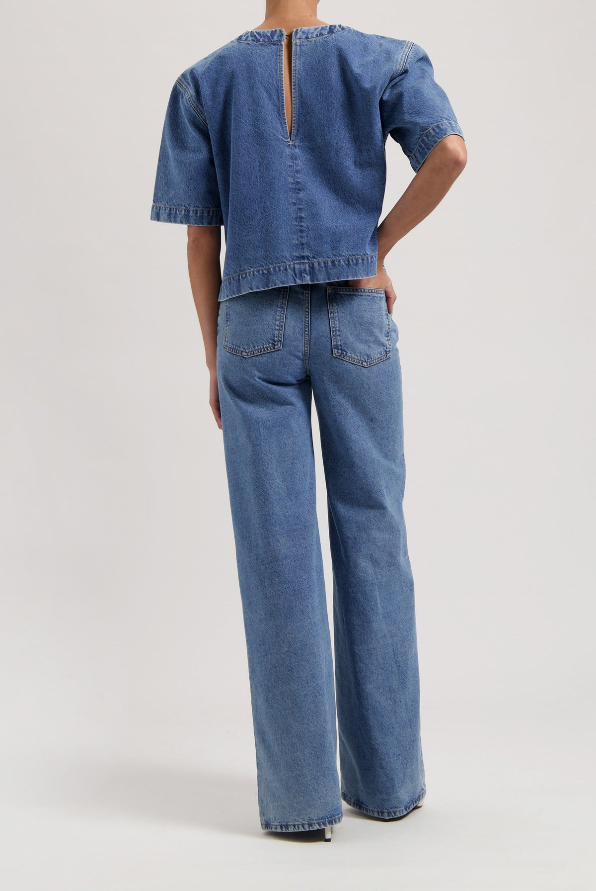 Back view of model wearing a matching light blue denim set with a short-sleeve top and wide-leg jeans.