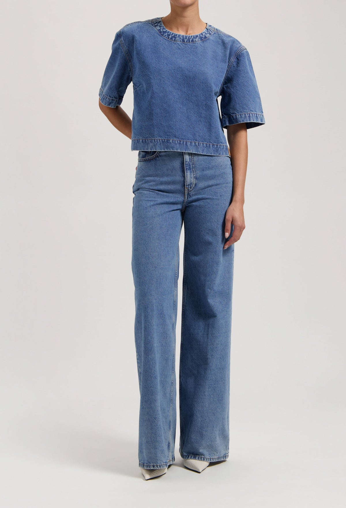 Model wearing blue denim two-piece outfit with short-sleeve top and wide-leg jeans, showcasing casual fashion style.