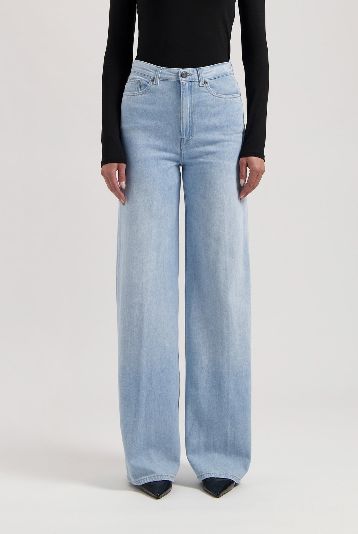Woman wearing light blue wide-leg jeans and a black long-sleeve top, showcasing casual fashion style.