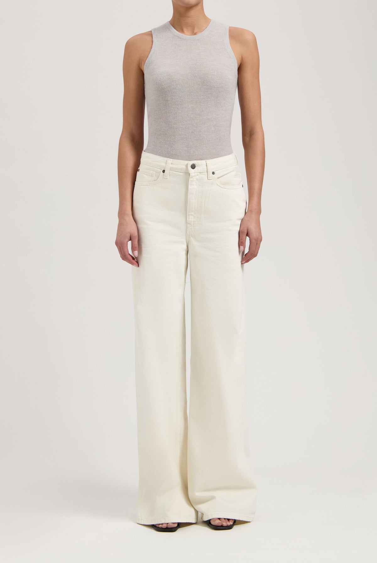 Woman wearing light gray sleeveless top paired with high-waisted, wide-leg white denim jeans, showcasing modern casual fashion.