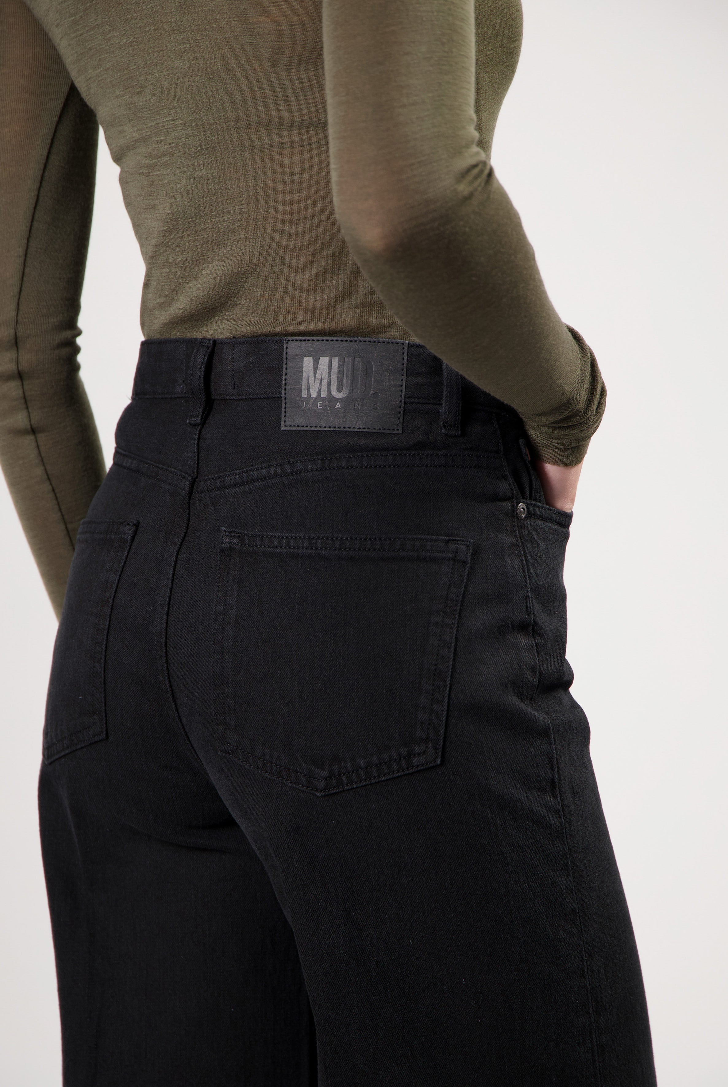 High-waisted black MUD Jeans made from organic cotton, featuring rear pockets and paired with an olive green long-sleeve top.