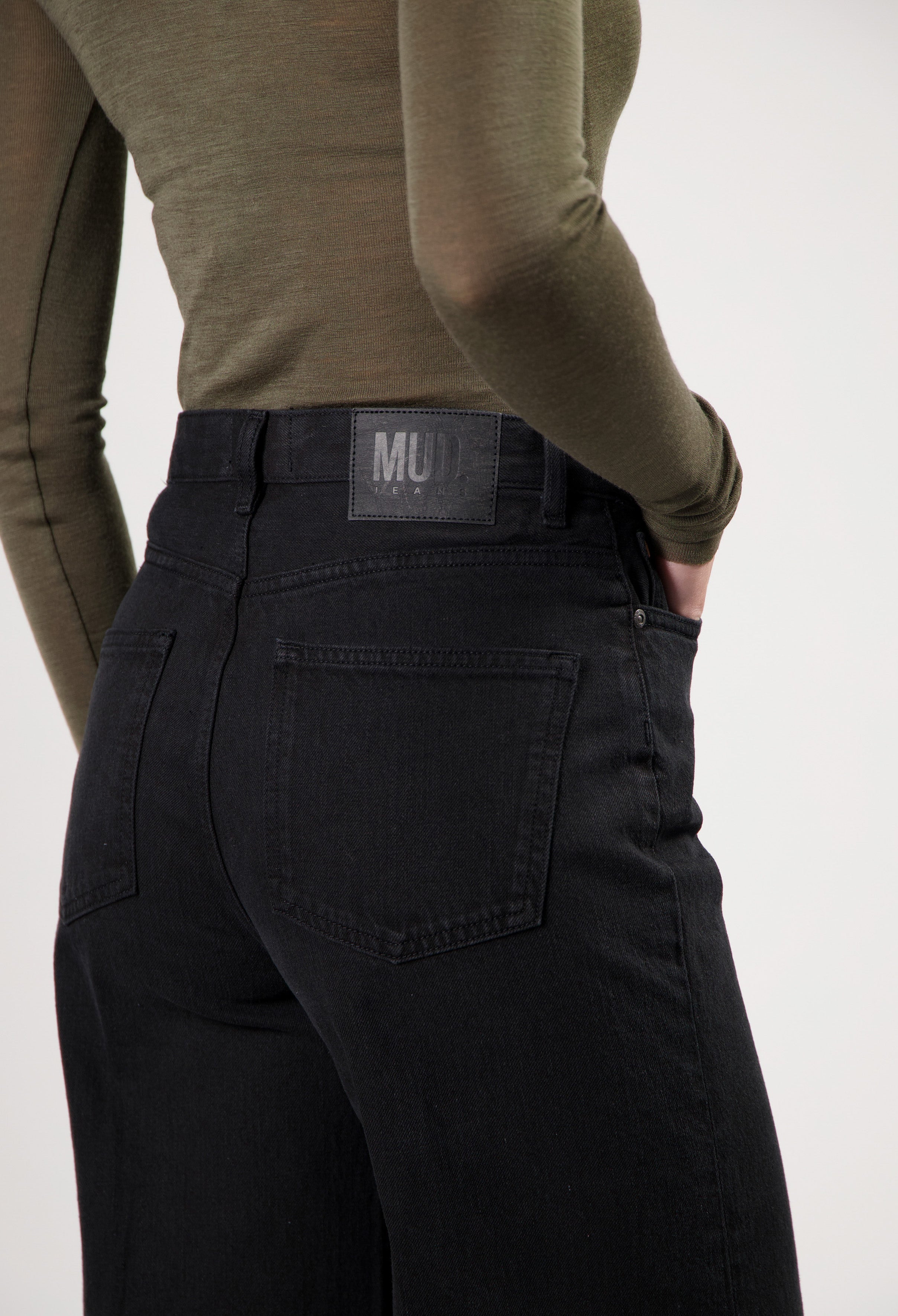 High-waisted black MUD Jeans made from organic cotton, featuring rear pockets and paired with an olive green long-sleeve top.