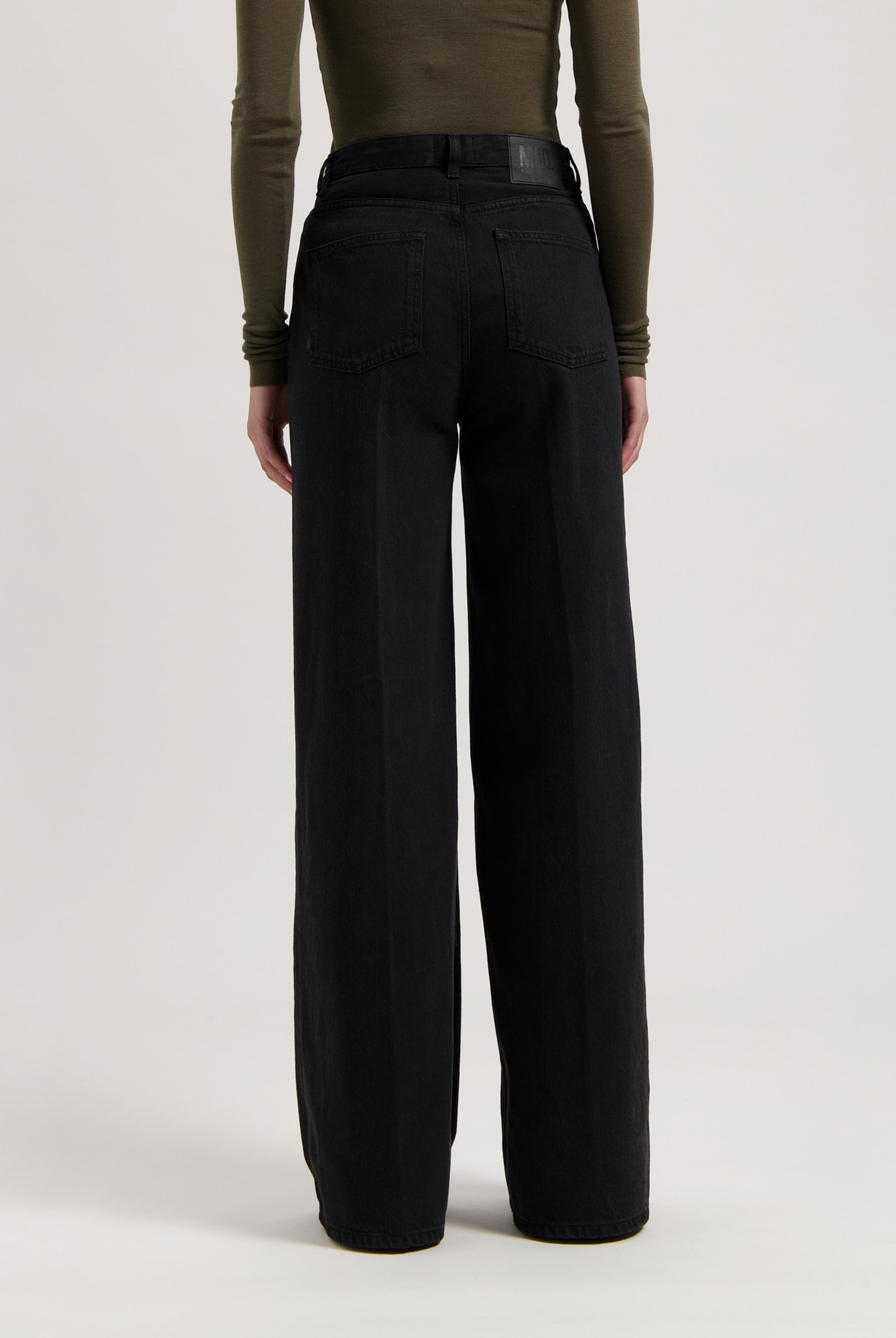 Wide-leg black denim jeans worn with a fitted olive green long-sleeve top, showcasing back pocket design.
