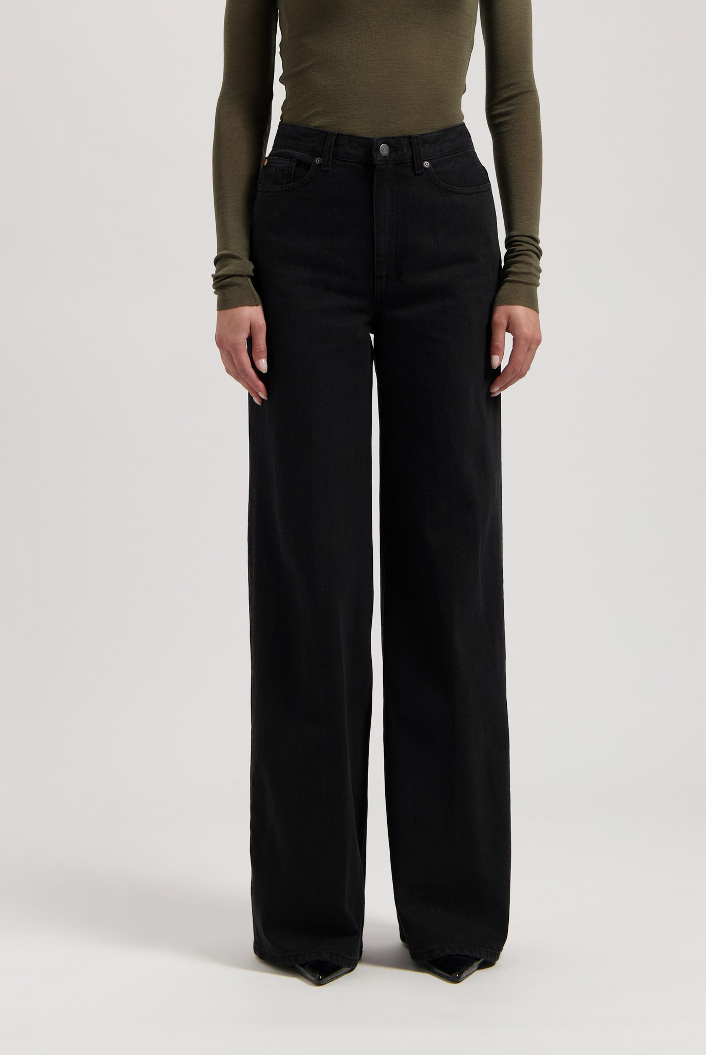 Woman wearing high-waisted, wide-leg black denim jeans paired with an olive green, long-sleeve fitted top.