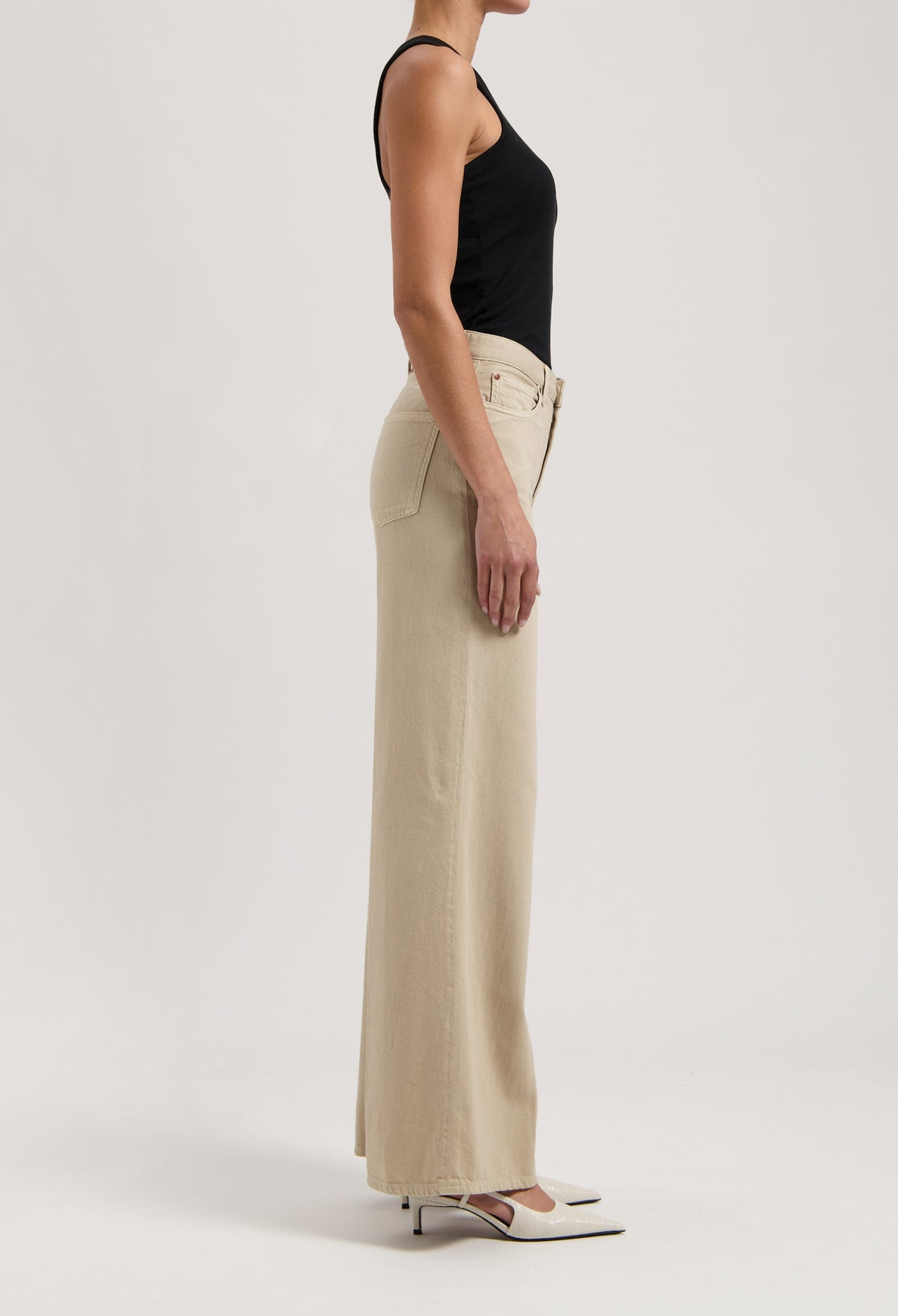A woman wearing a black tank top and beige wide-leg pants, highlighting a side profile of minimalist fashion style.