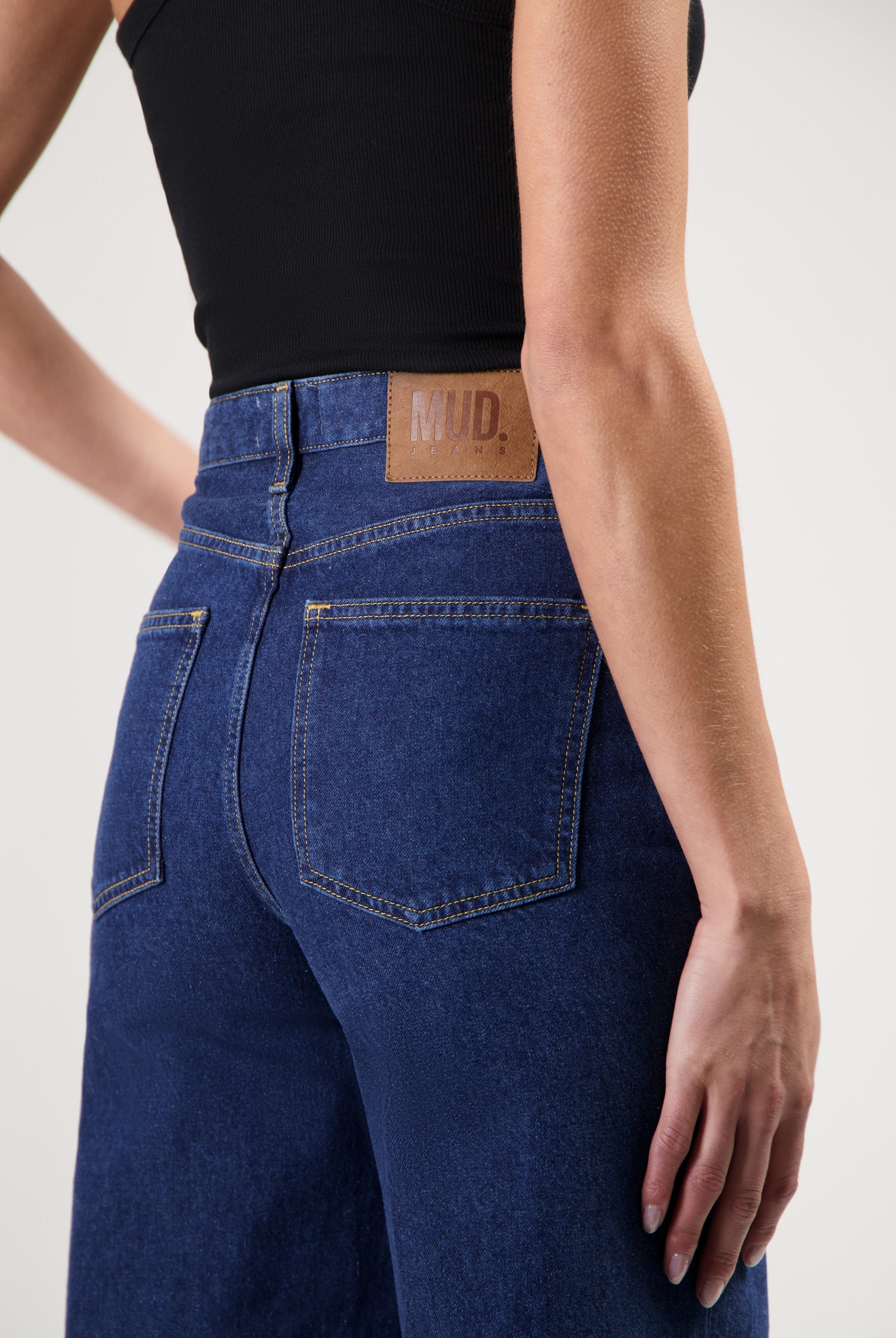 Close-up of indigo blue MUD Jeans made from organic cotton, showing back pockets and branding, paired with a black tank top.