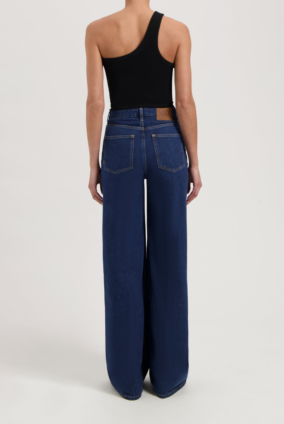 Wide-leg blue denim jeans from MUD Jeans, made from organic cotton, shown worn with a sleeveless black top.