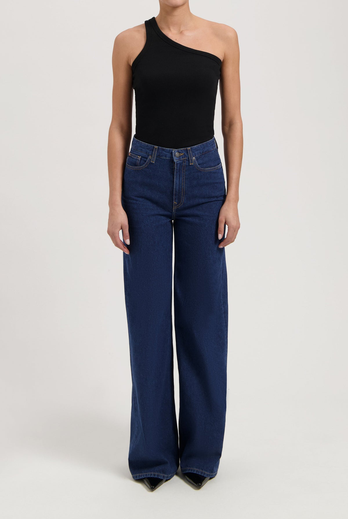 Wide-leg high-waisted jeans in deep blue, paired with a black one-shoulder top, showing a casual yet stylish look.