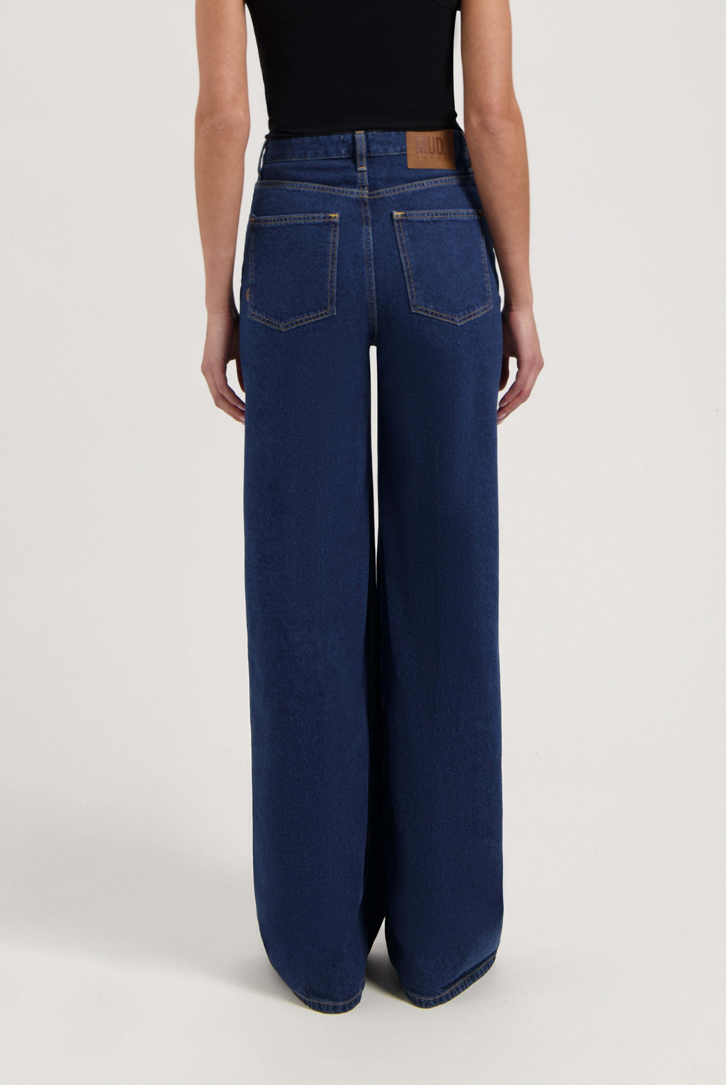 Wide-leg blue denim jeans from MUD Jeans made from organic cotton, shown from the rear, paired with a sleeveless black top.