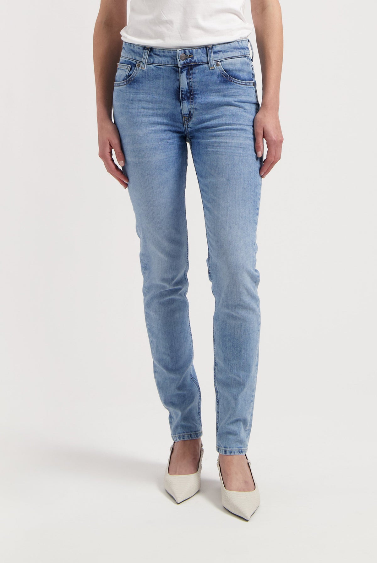 Light blue slim-fit jeans made from denim, paired with a white top and pointed white heels, showcased on a person standing.