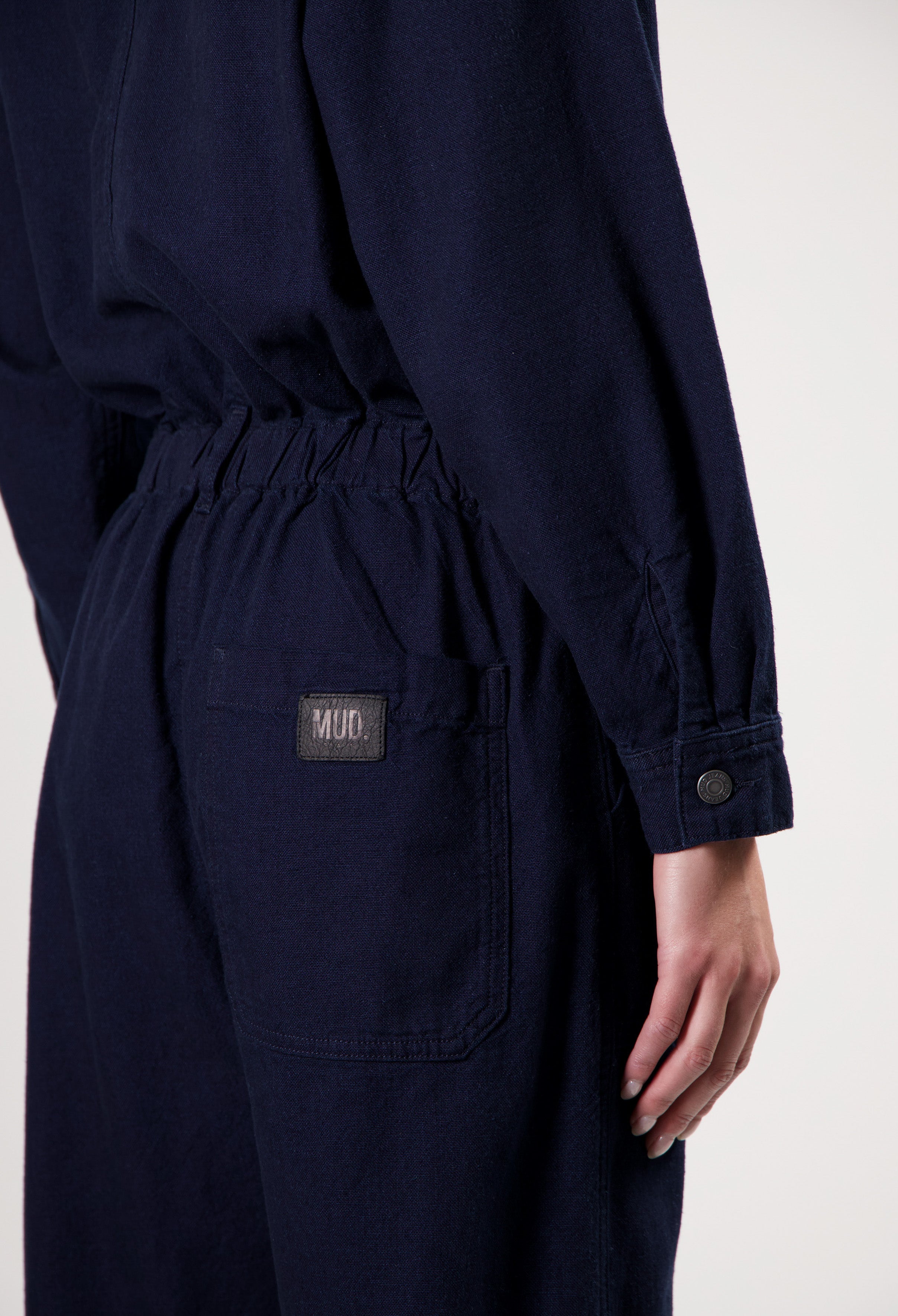 Navy blue MUD denim jumpsuit with elastic waistband and pocket detailing, long sleeves with button cuffs.