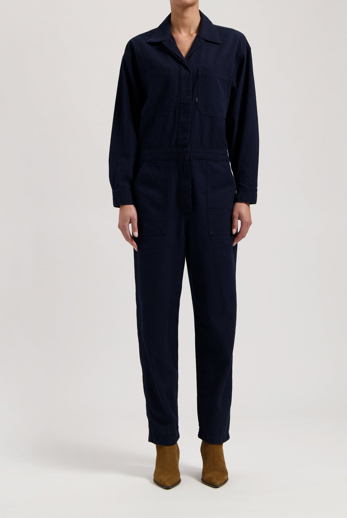 Navy blue cotton jumpsuit with button front and long sleeves, paired with brown suede ankle boots.