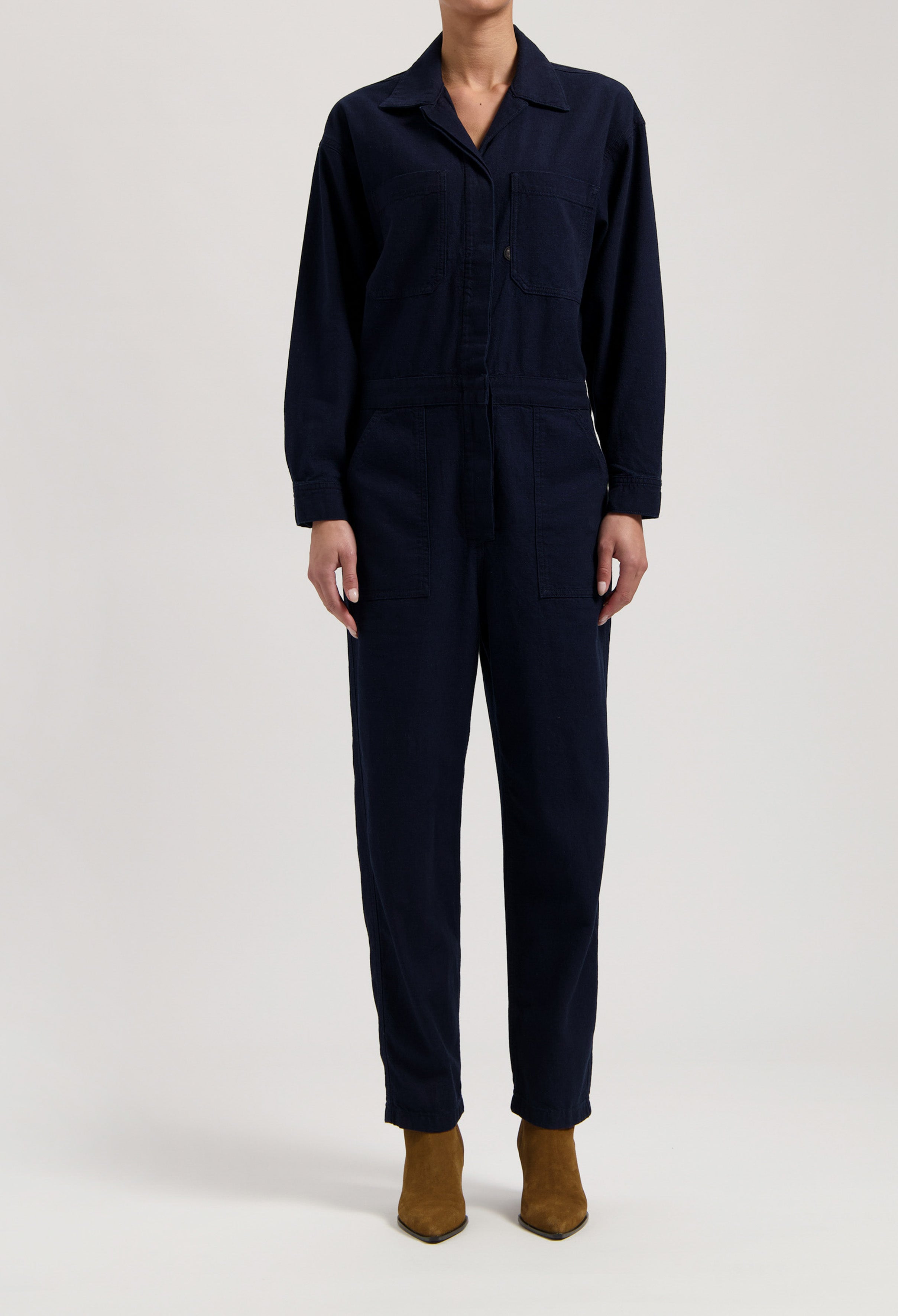 Navy blue cotton jumpsuit with button front and long sleeves, paired with brown suede ankle boots.