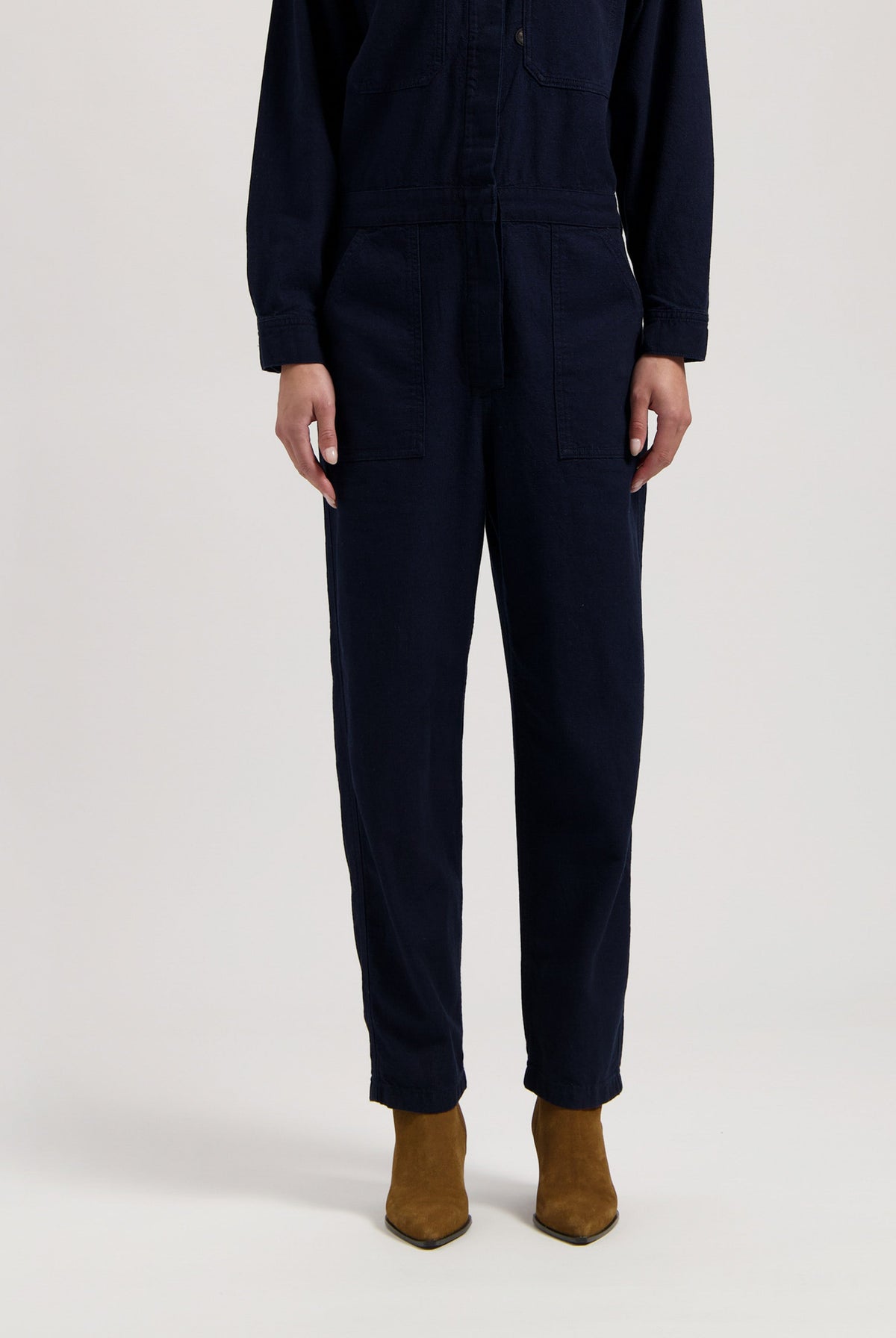 Dark navy long-sleeve jumpsuit with front pockets, paired with brown suede ankle boots.