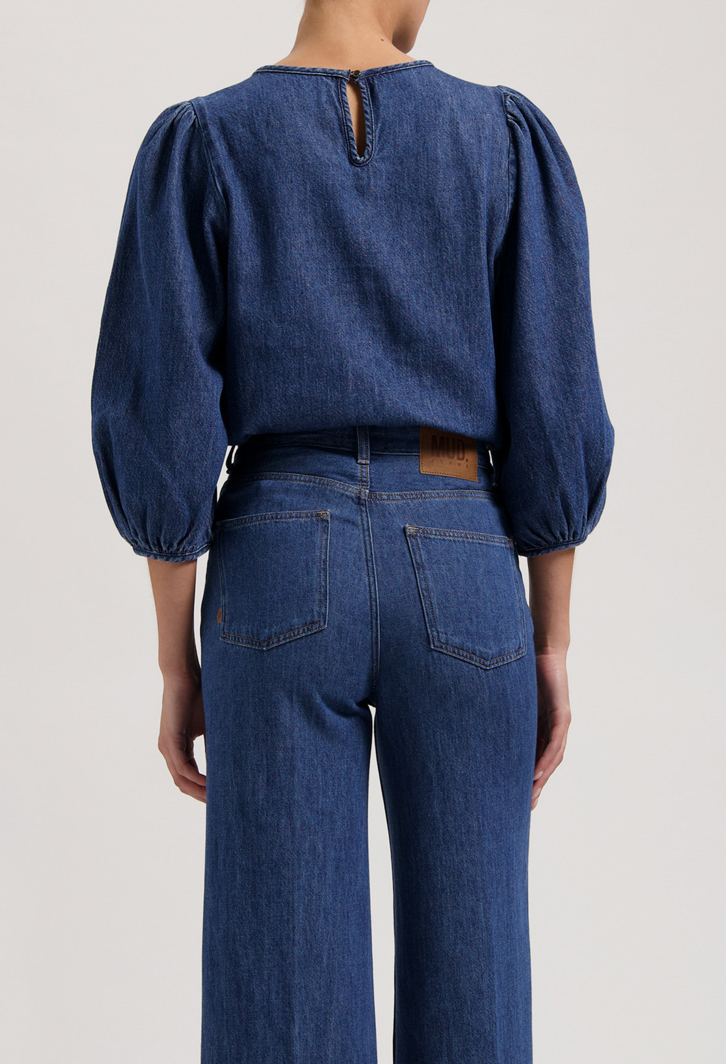 Dark blue denim outfit with balloon-sleeve top and wide-leg jeans, showcasing sustainable fashion by MUD Jeans.