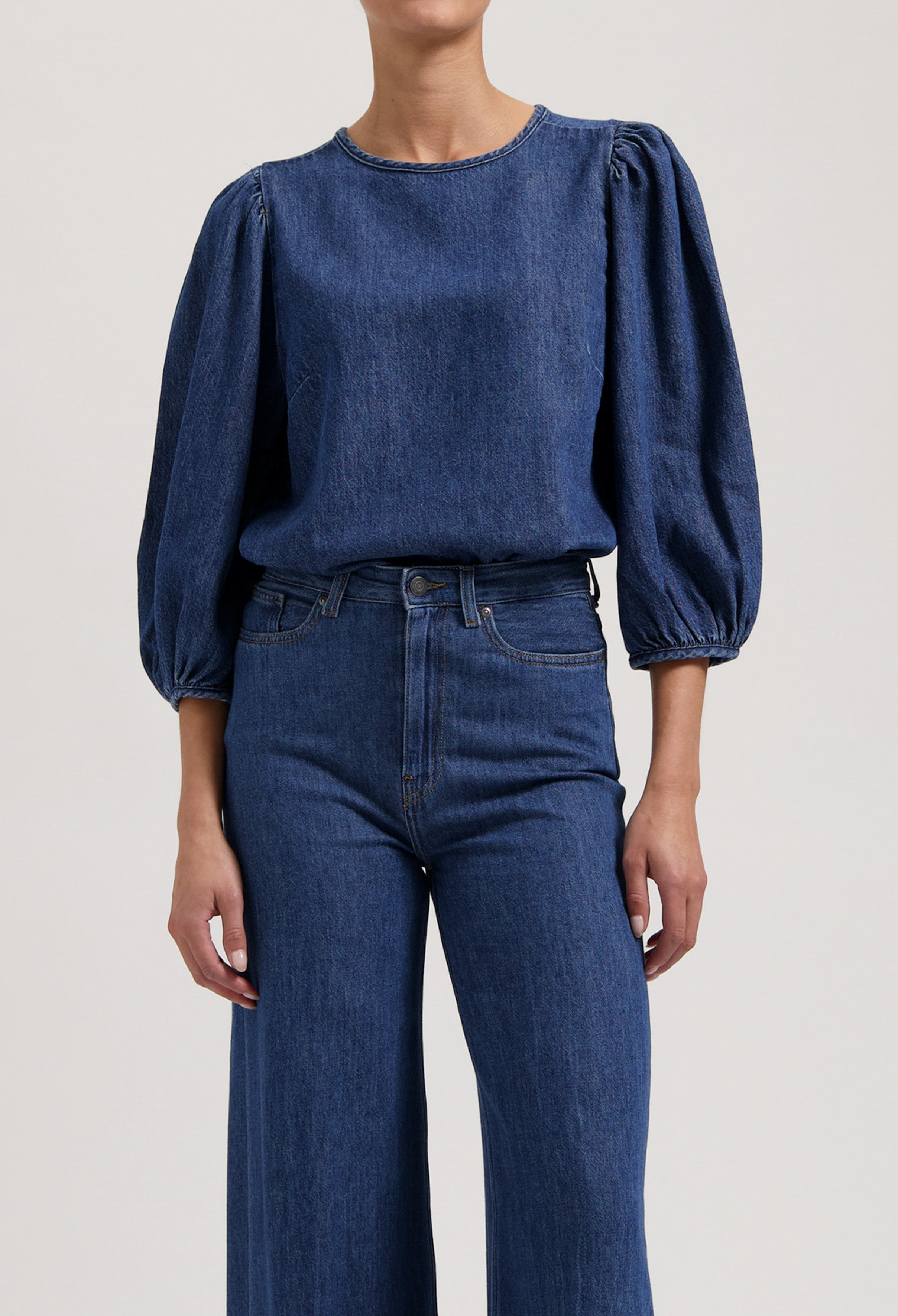 Denim top with puffed sleeves worn with high-waisted, wide-leg jeans, showcasing casual blue denim attire.