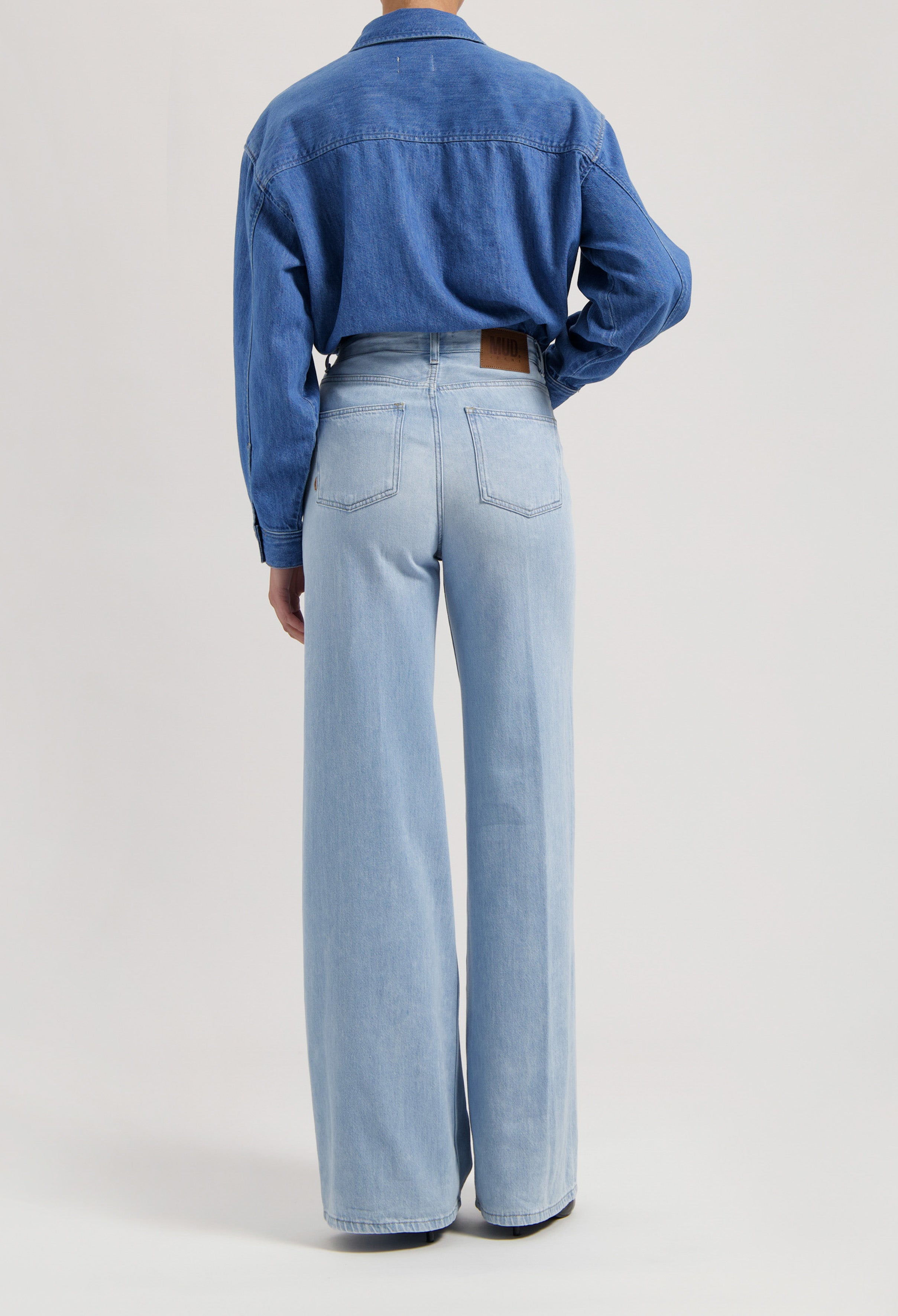 Back view of light blue high-waisted wide-leg jeans with a dark blue denim jacket, emphasizing sustainable fashion style.