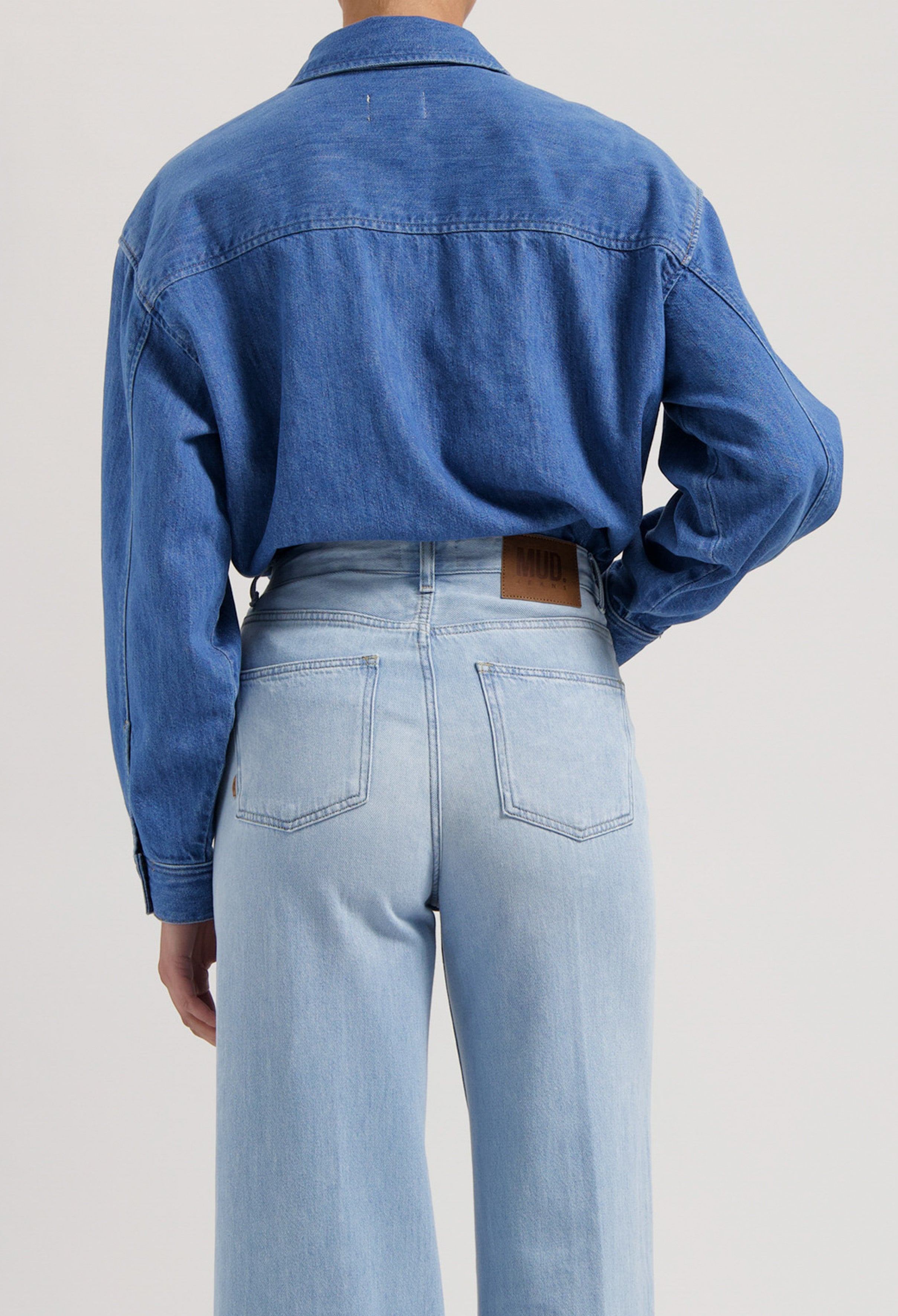 Back view of sustainable MUD Jeans, light blue high-waisted wide-leg denim paired with a classic blue denim shirt.
