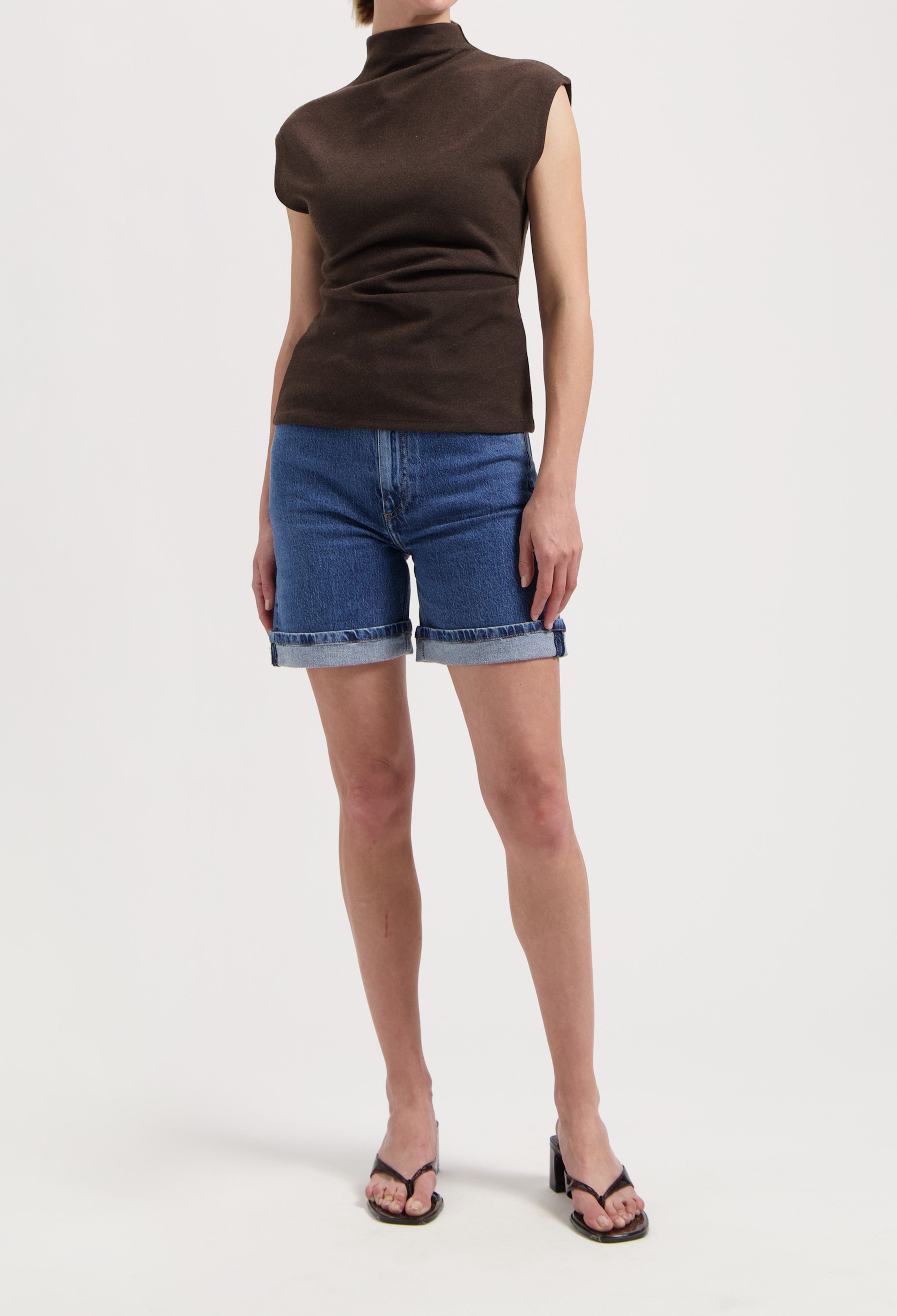 Brown sleeveless turtleneck paired with rolled-up denim shorts and black heeled sandals, showcasing casual summer style.