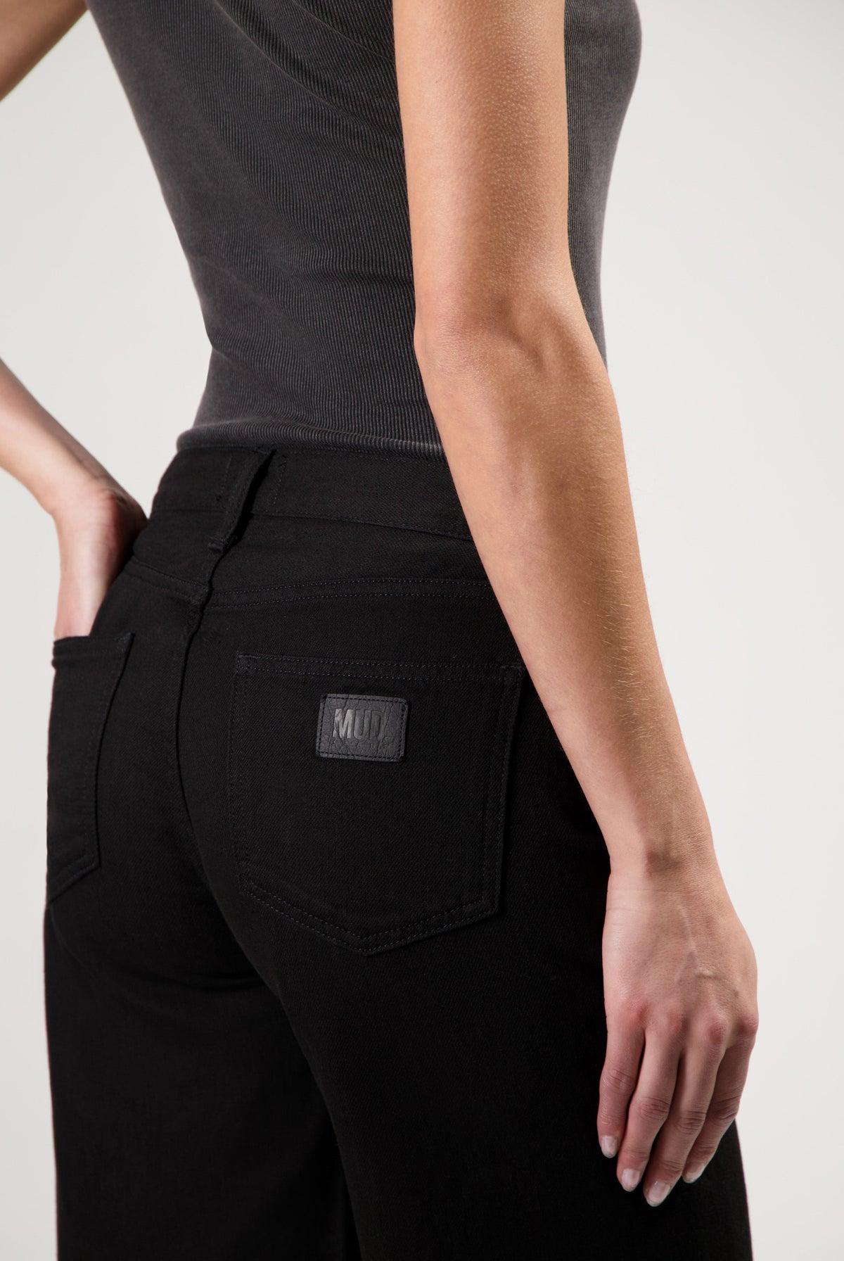 Black MUD jeans made from organic cotton, featuring a high-waisted slim-fit design, paired with a sleeveless dark gray top.