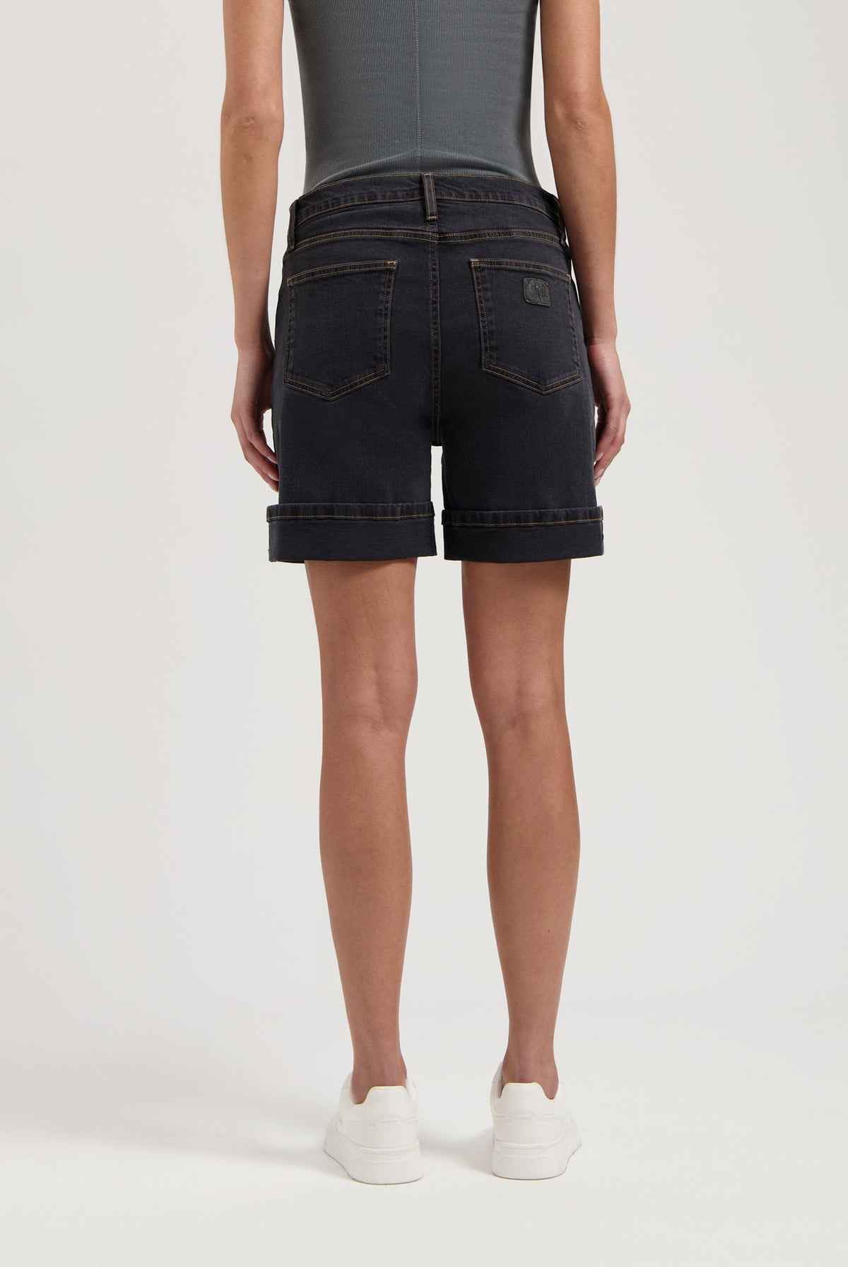 Dark denim shorts with rolled cuffs worn with a fitted gray top, highlighting casual summer fashion in white sneakers.