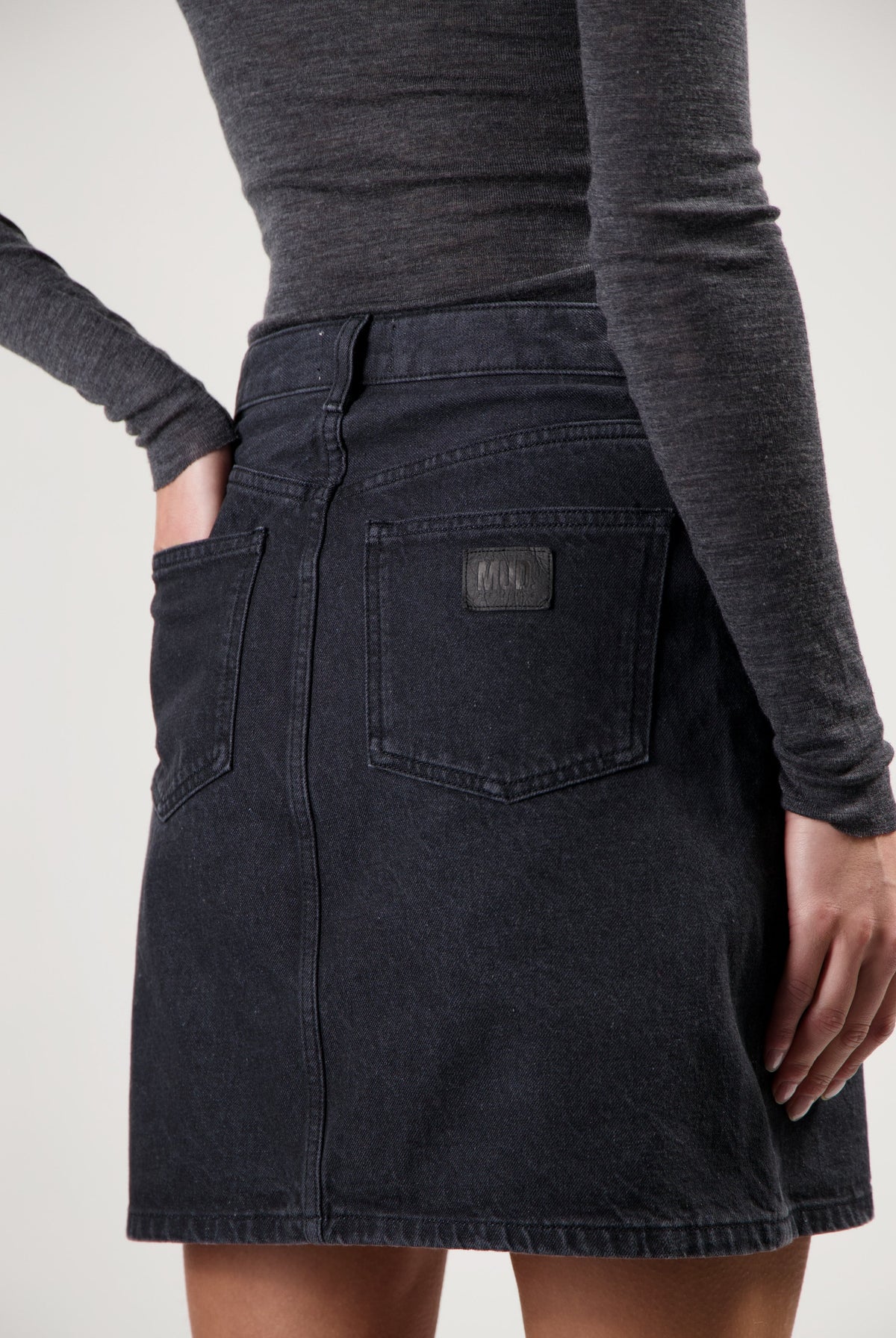 Dark denim mini skirt by MUD Jeans with back pockets, paired with a fitted long-sleeve gray top for a casual look.