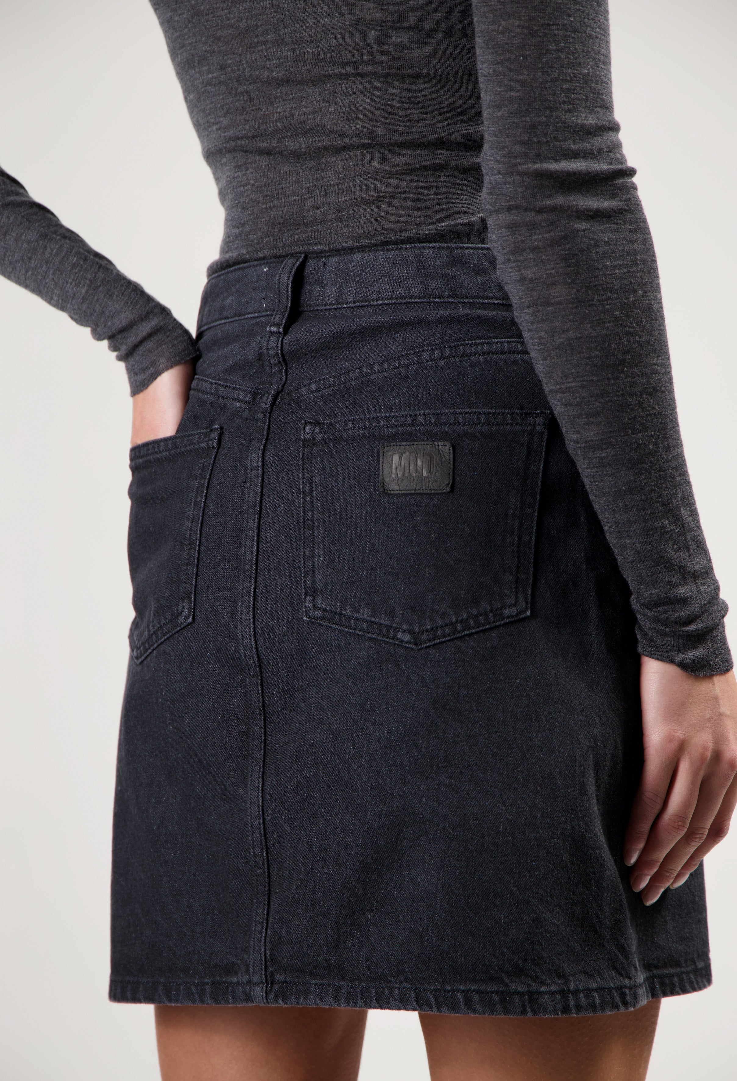 Dark denim mini skirt by MUD Jeans with back pockets, paired with a fitted long-sleeve gray top for a casual look.