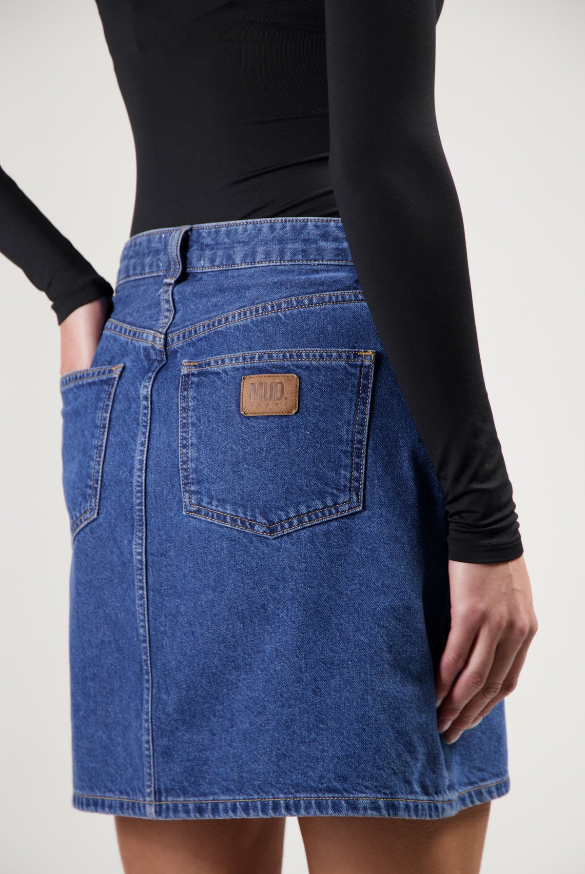 Sustainable blue denim skirt by MUD Jeans, featuring deep blue fabric, back pockets, and paired with a fitted black top.